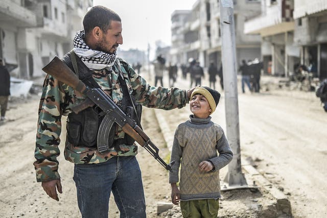 A Kurdish fighter walks with his child in Kobani after Isis was driven out of the strategic Syrian border town