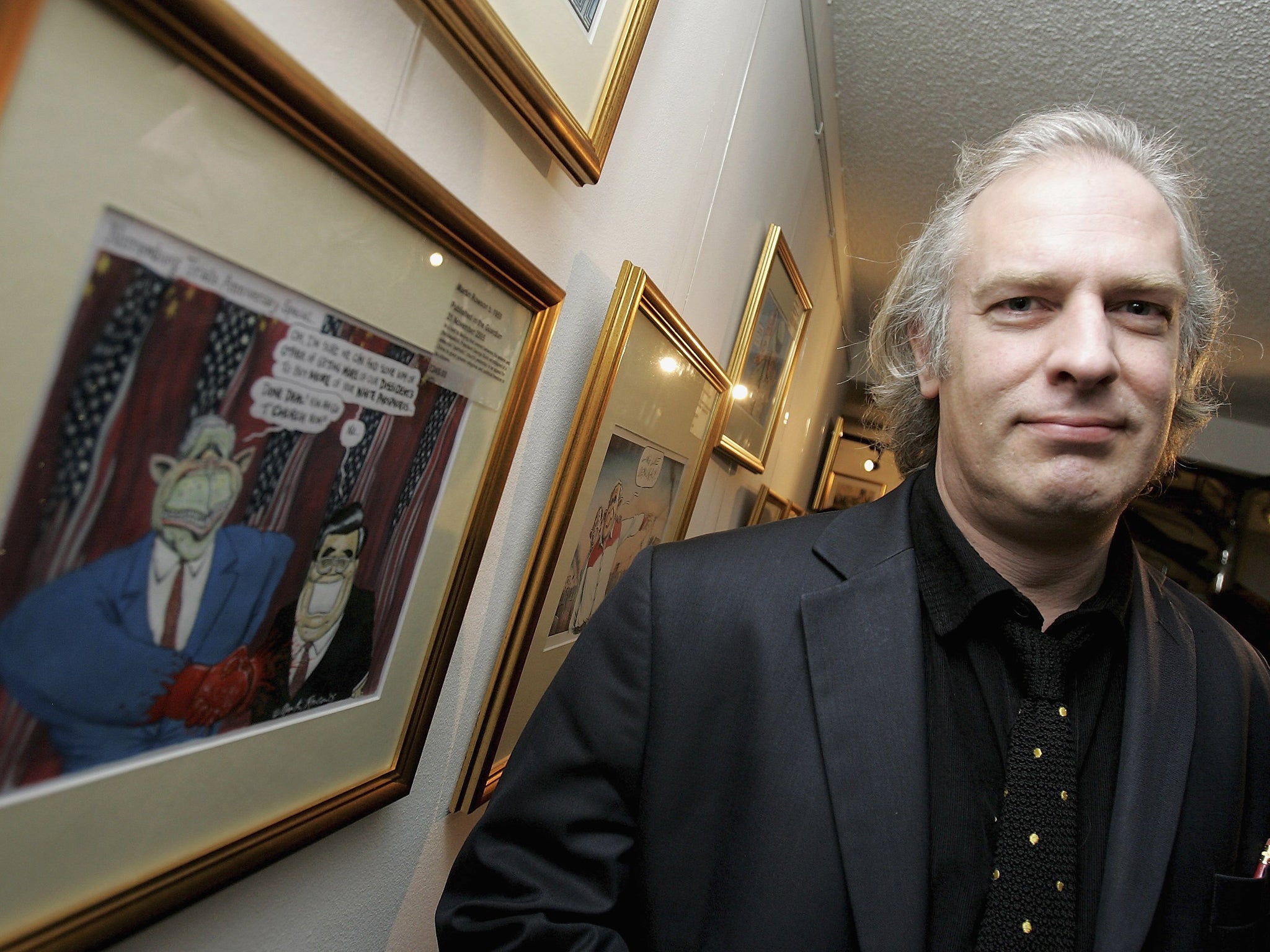 Cartoonist Martin Rowson poses with one of his cartoons at the Private View for "Misunderestimating The President Through Cartoons", an exhibition of caricatures of the President by leading UK and US political artists, at the Political Cartoon Gallery on