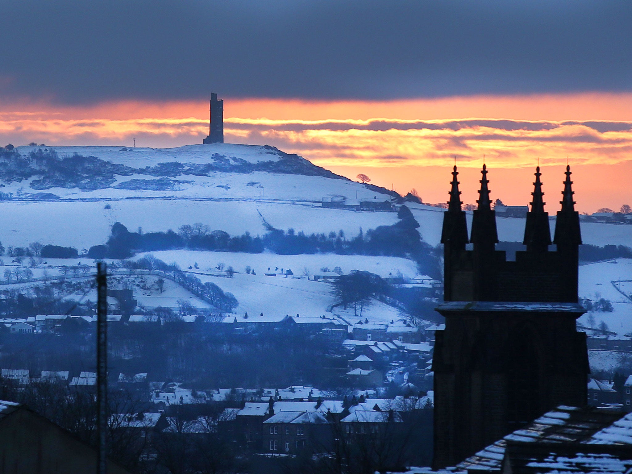 The sun rises behind the Victora Tower on a snow covered Castle Hill in Huddersfield