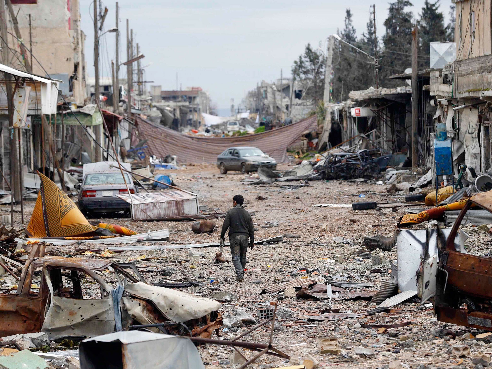 A man walks in a street with abandoned vehicles and and damaged buildings in the northern Syrian town of Kobani