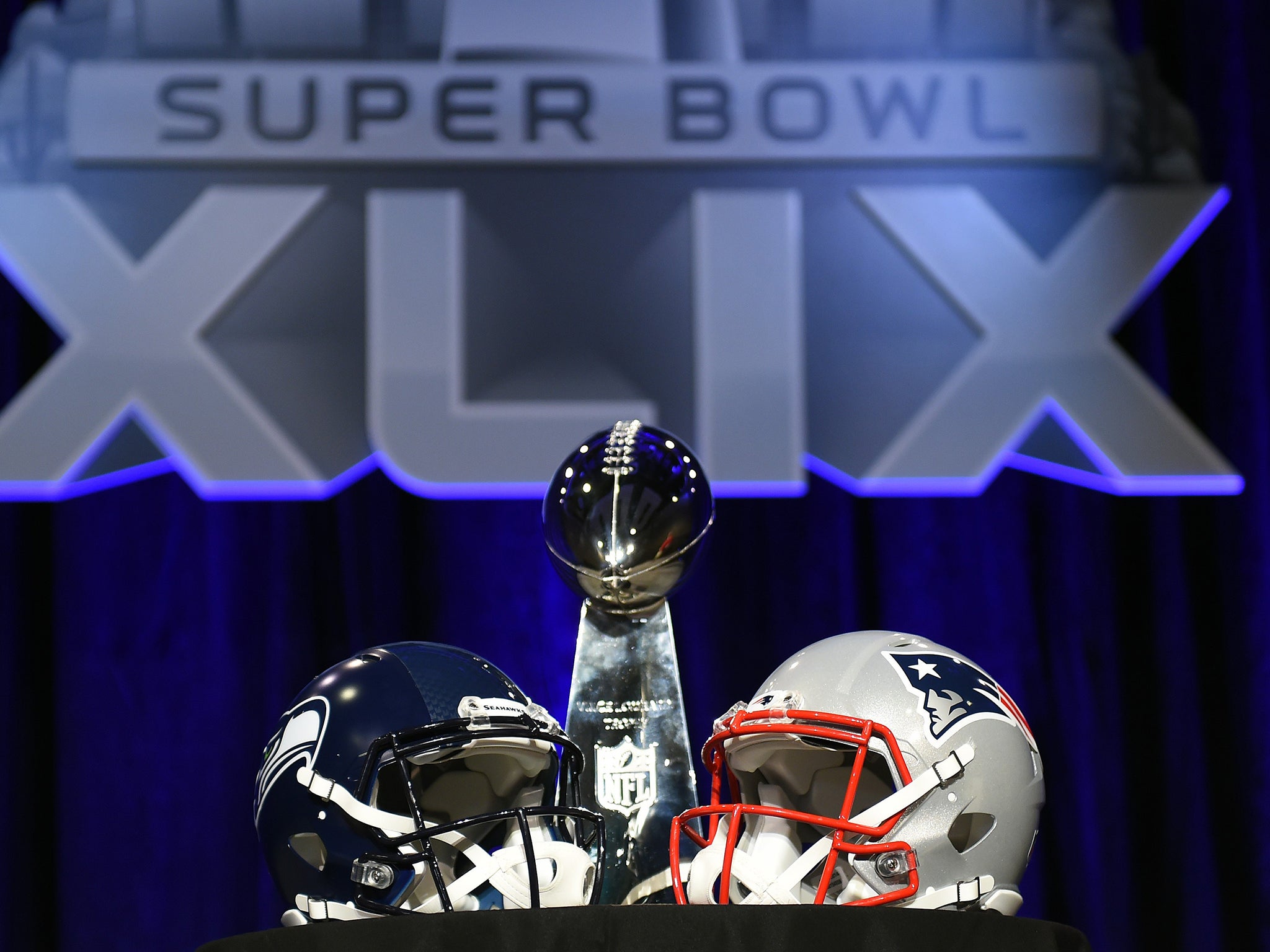 The Vince Lombardi Trophy sits alongside the helmets of the Seattle Seahawks (L) and New England Patriots