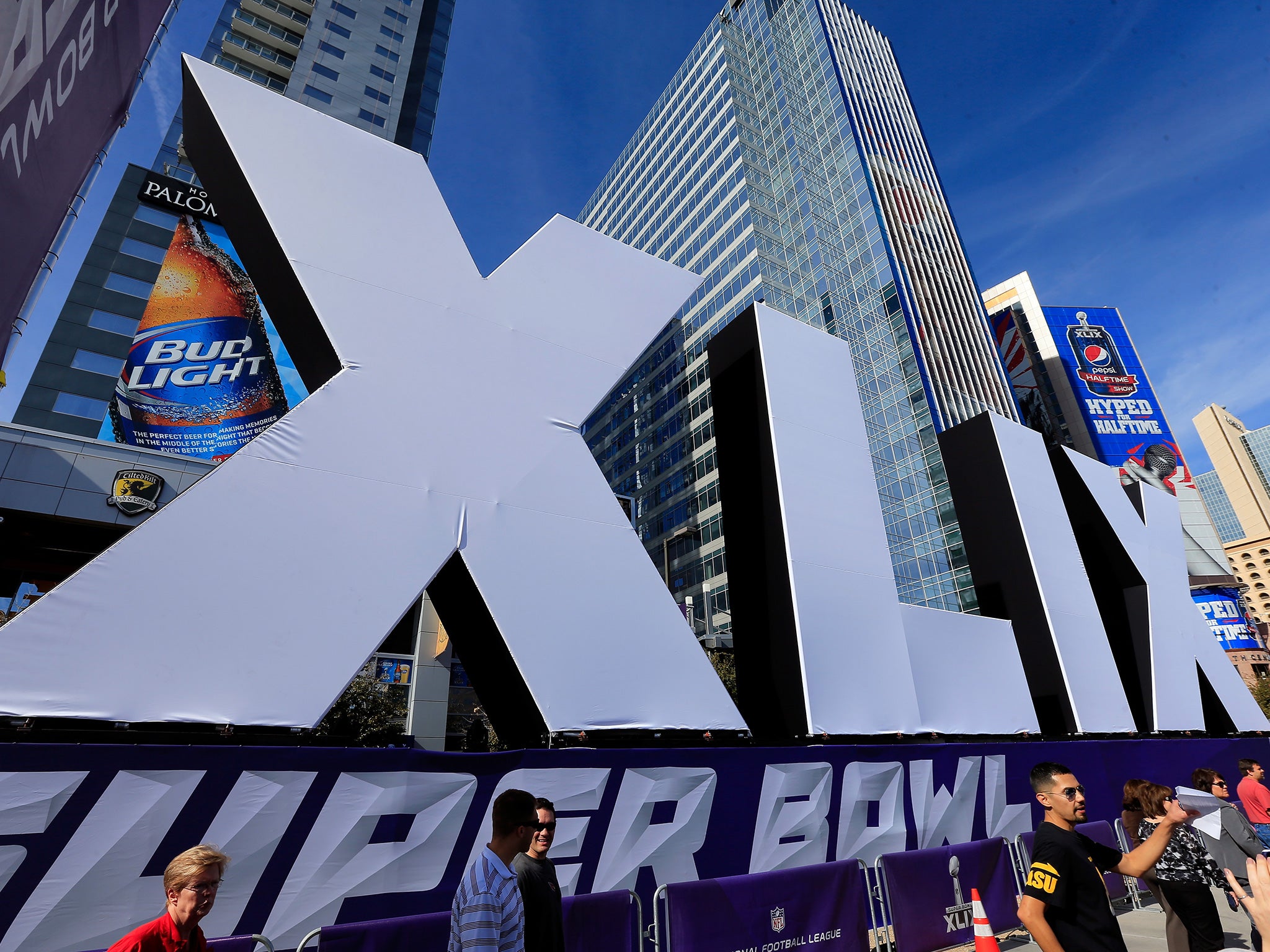 People walk past the logo for the Super Bowl XLIX