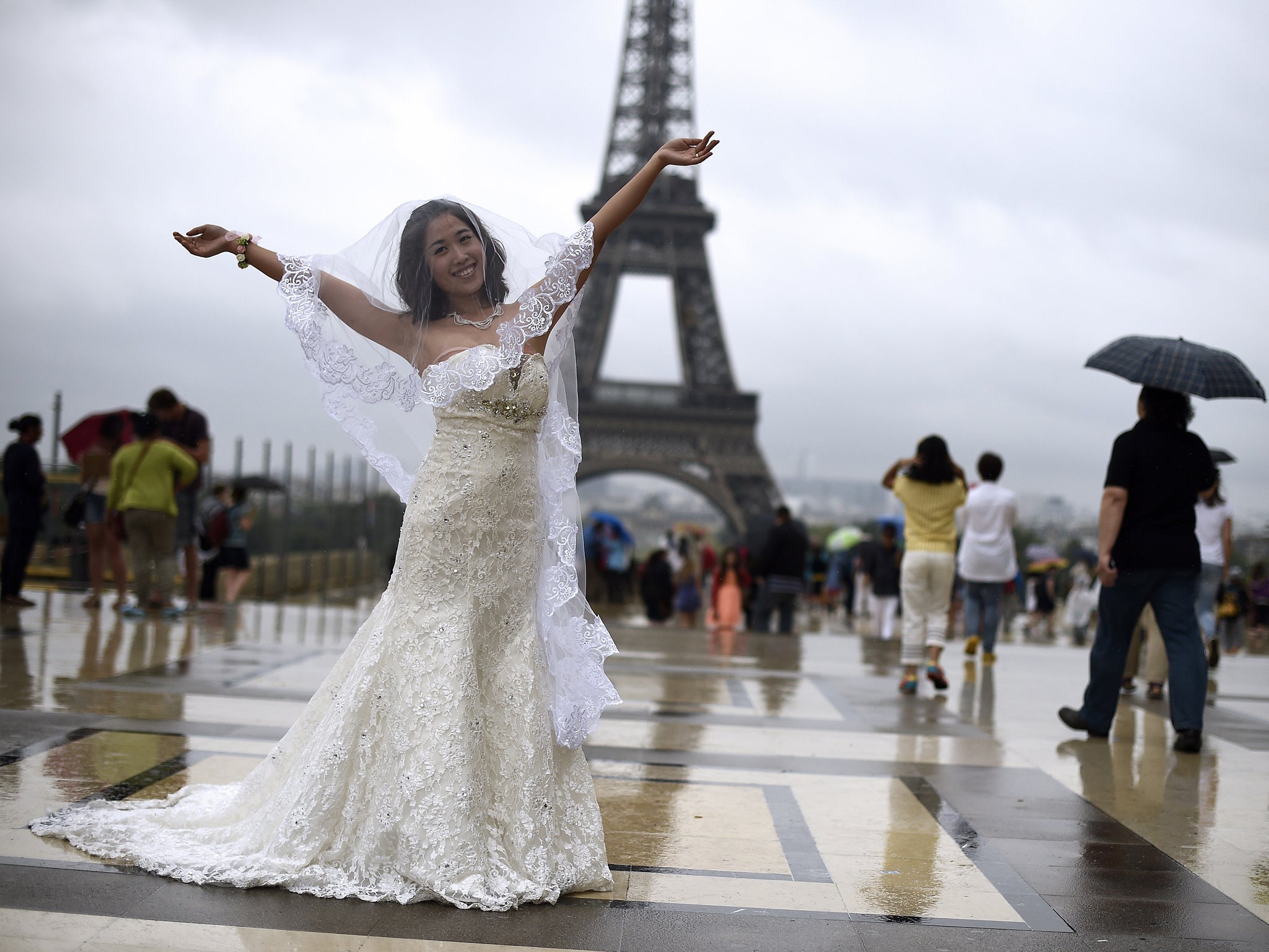 A bride gestures as she poses under the rain on the Trocadero esplanade in front of the Eiffel Tower in Paris on August 8, 2014