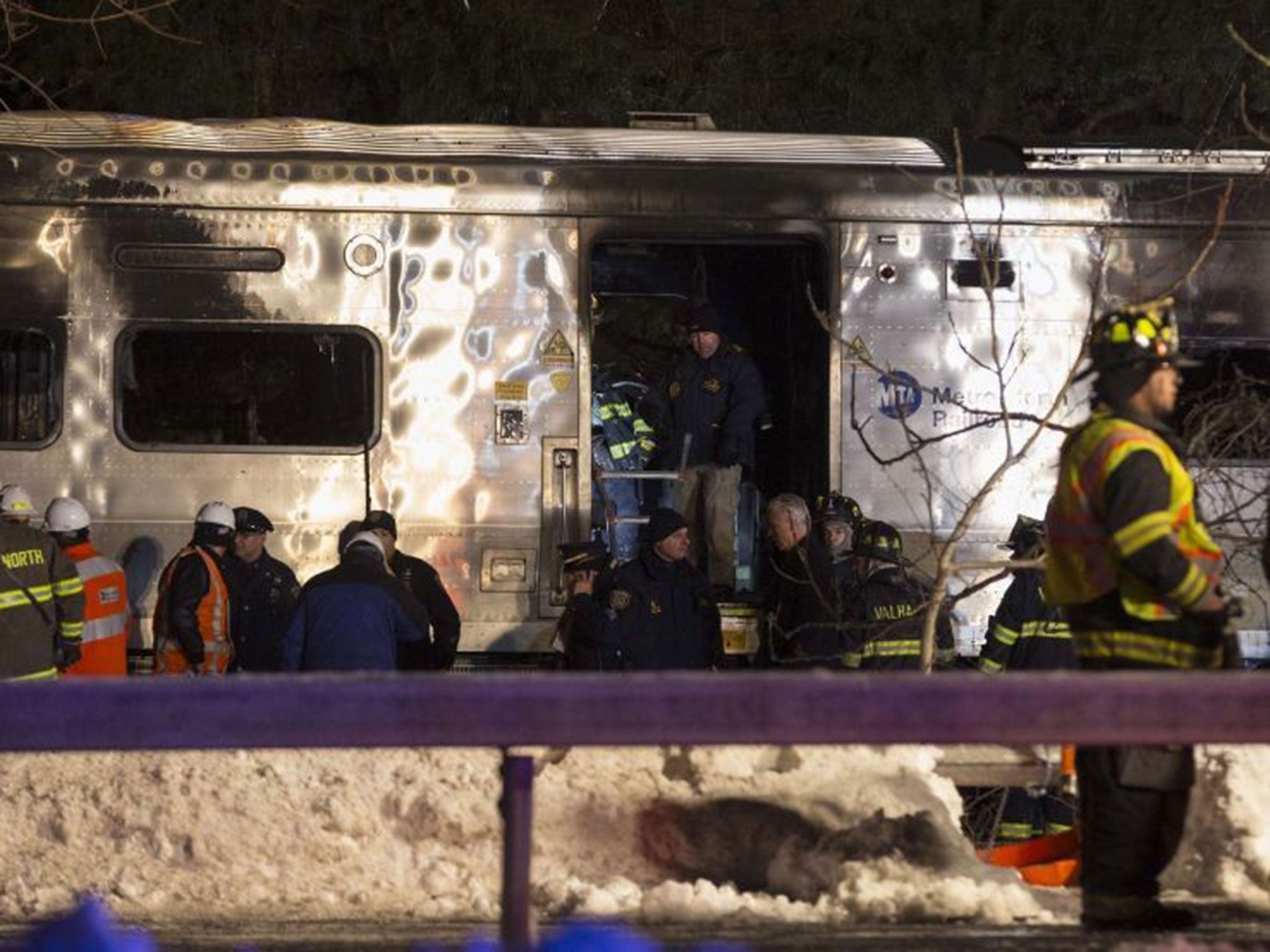 Emergency workers stand in and around a burnt Metropolitan Transportation Authority (MTA) Metro North Railroad commuter train near the town of Valhalla, New York