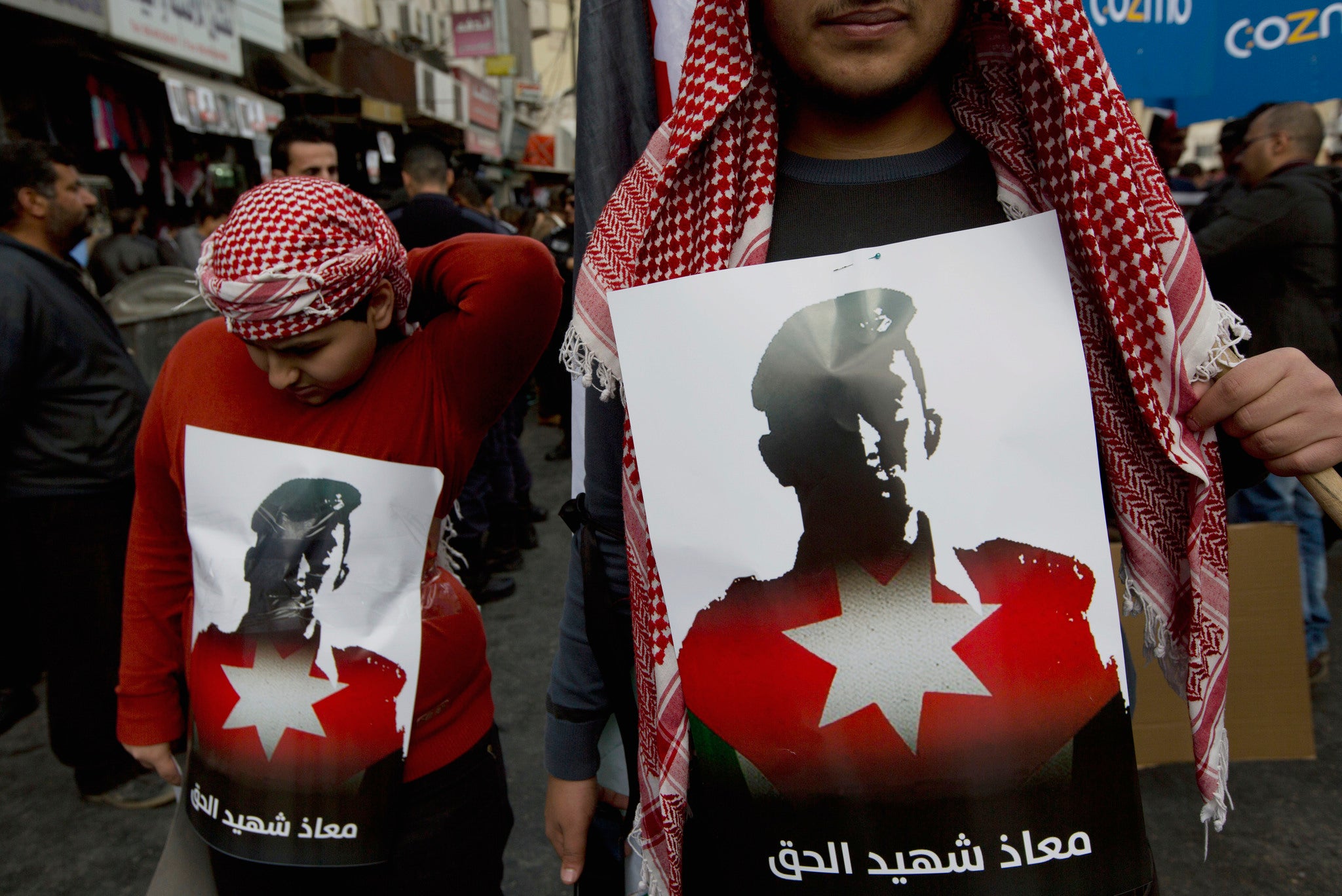 Two Jordanian demonstrators carry posters with pictures of slain Jordanian pilot, Lt. Muath al-Kaseasbeh, and Arabic that reads, "Muath is the martyr of the right" .