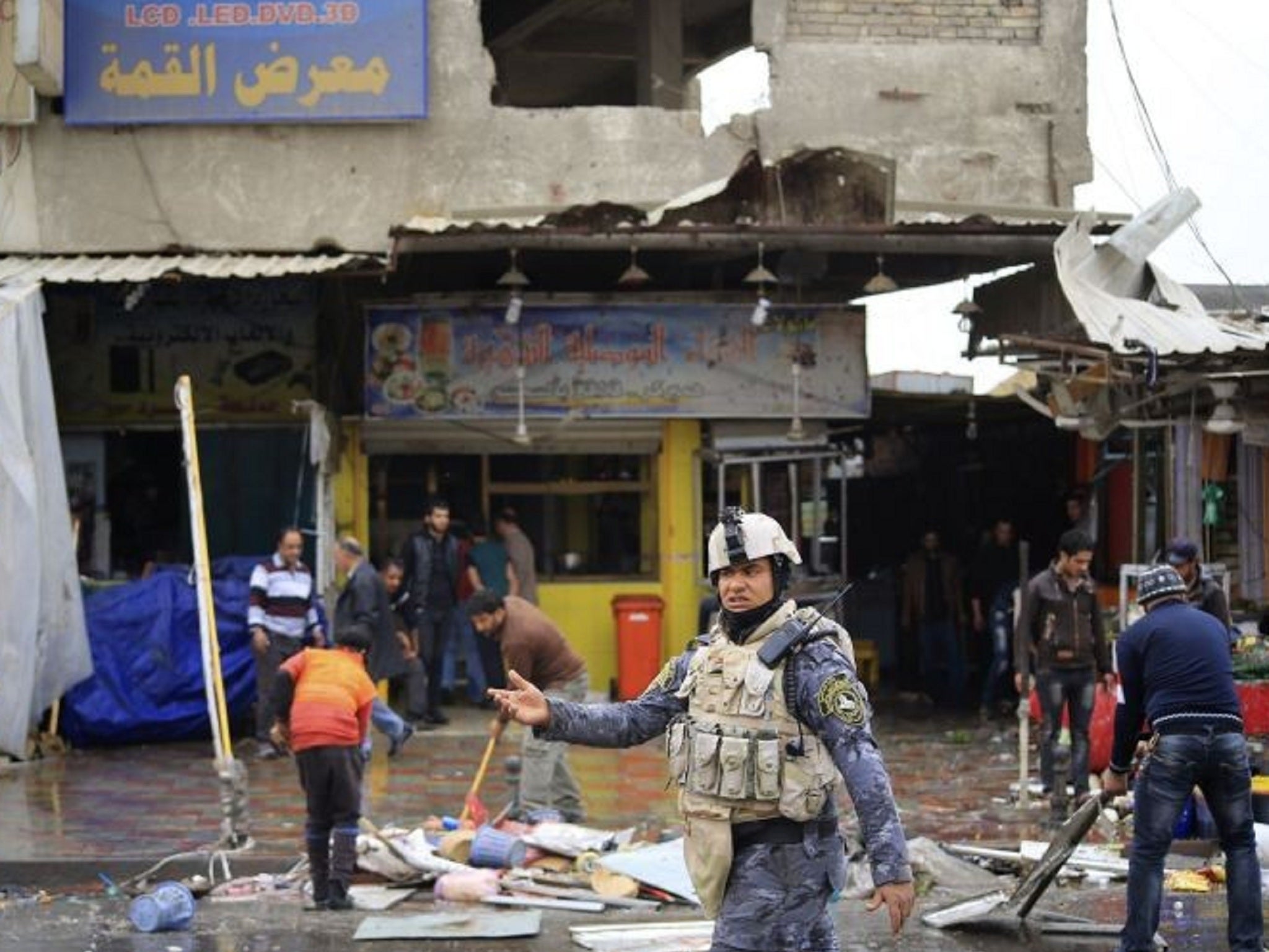 Iraqi policeman helps usher pedestrians away from the bombing scene in New Baghdad