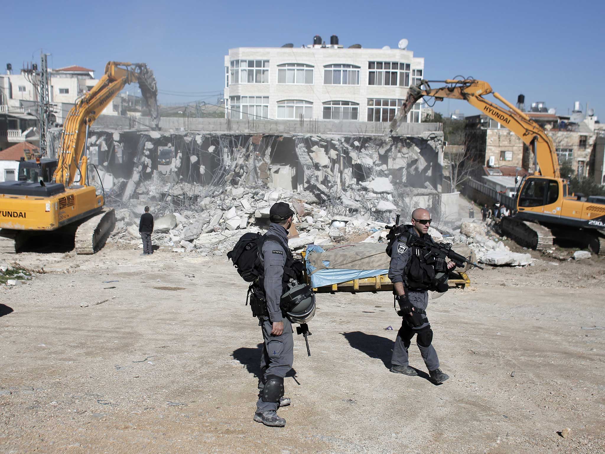 Members of the Israeli security forces stand guard as bulldozers hired by the Jerusalem municipality destroy a Palestinian house