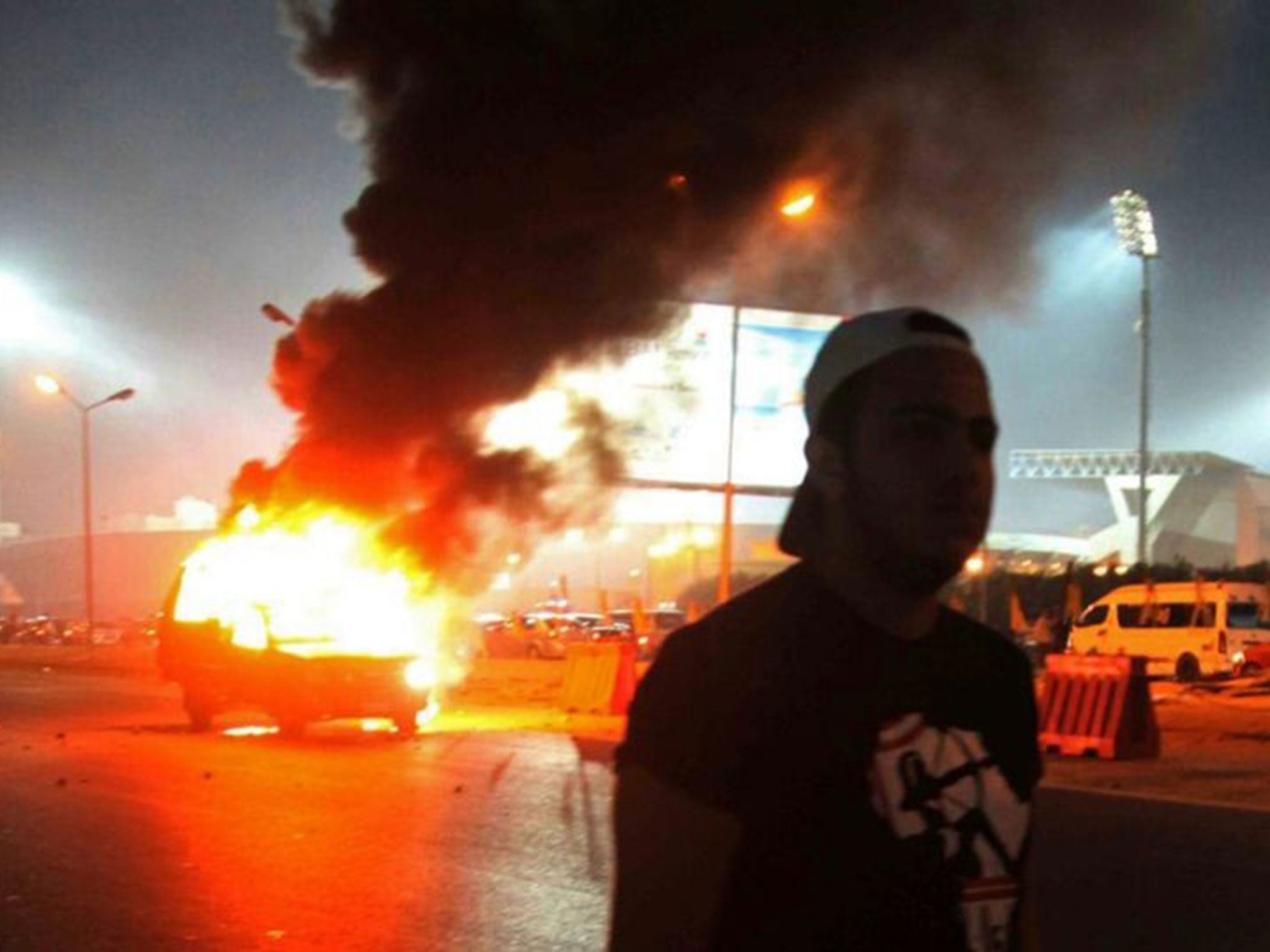 A football fan by a burning police car after clashes with security forces outside the Air Defence Stadium on 8 February