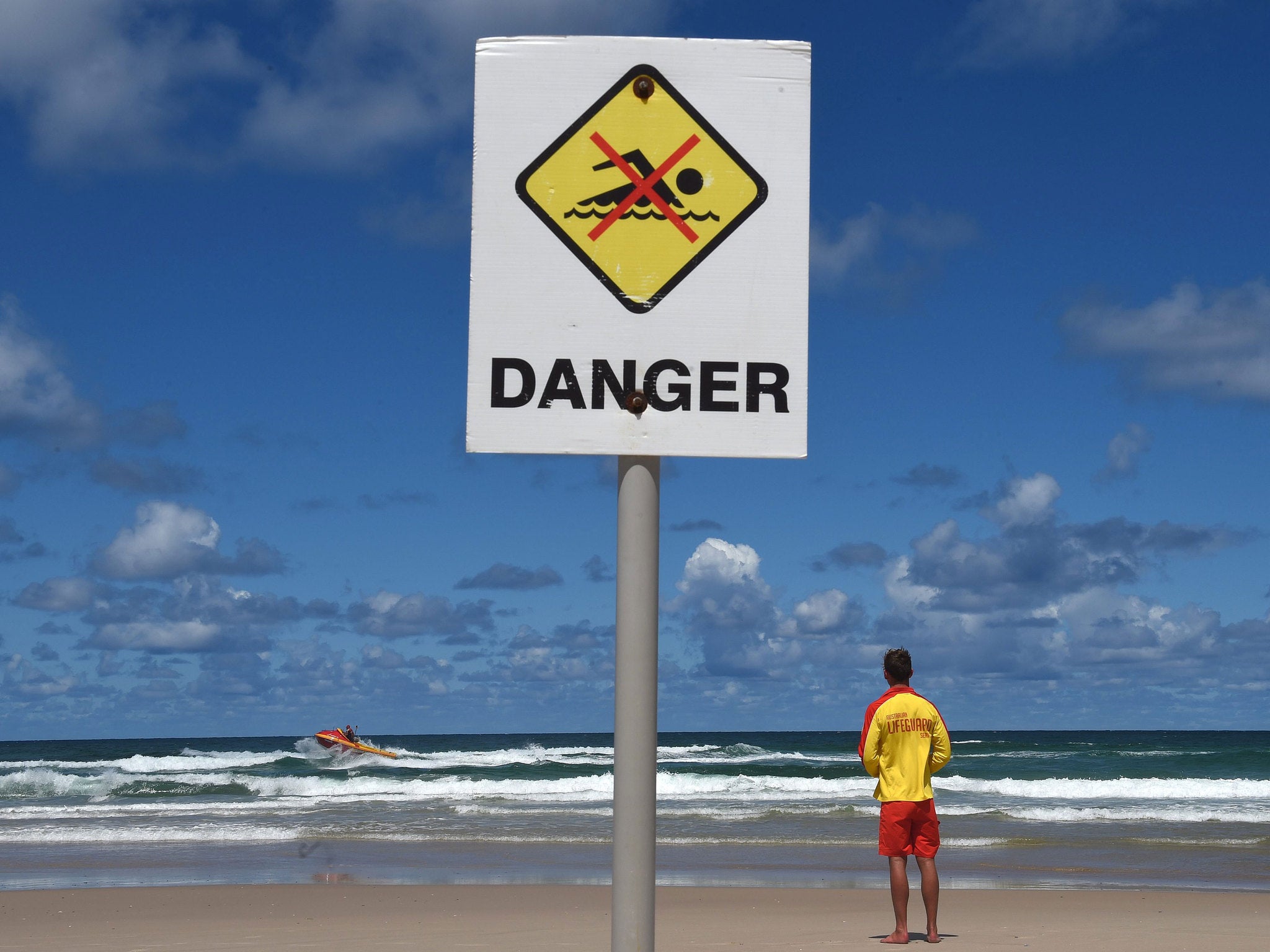 A lifeguard stands on Shelly Beach while a search rescue boat scours the sea