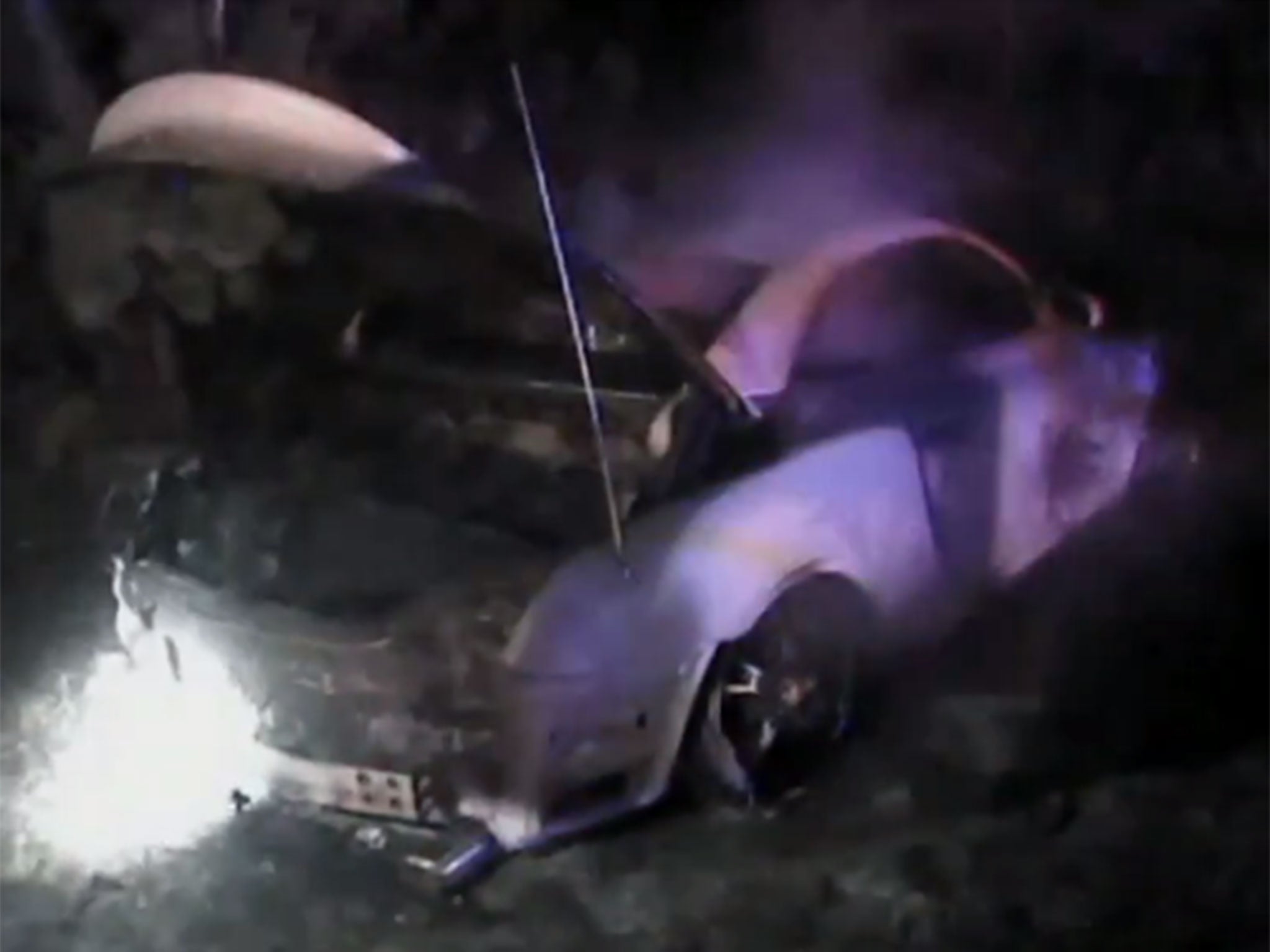 As the policemen pull the driver out of the vehicle, the driver's legs can be seen engulfed in flames.