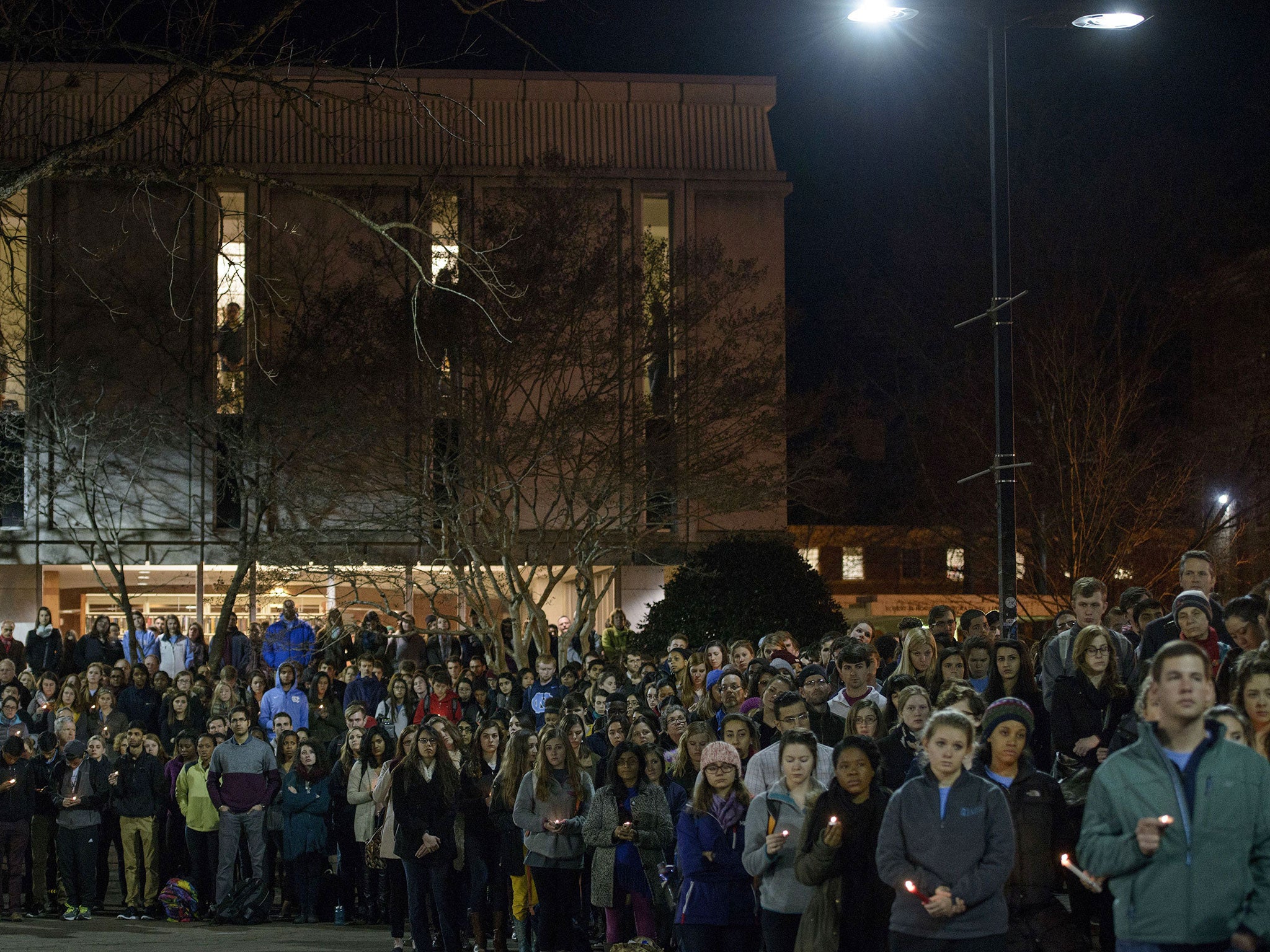 People listen to speakers and hold candles during the vigil