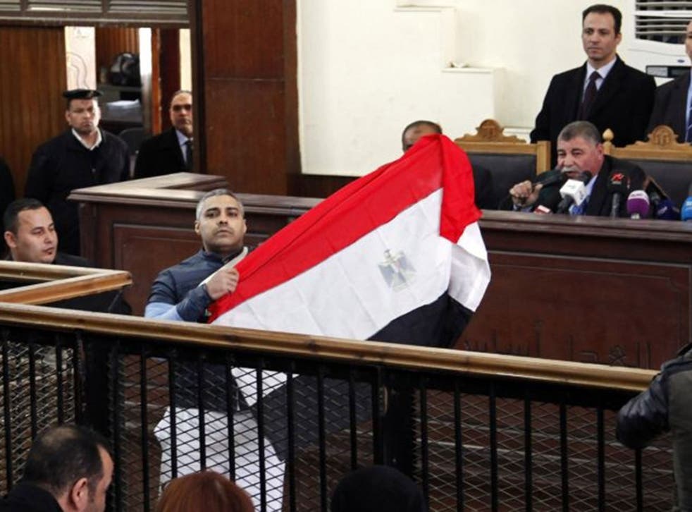 Al Jazeera journalist Mohamed Fahmy raises an Egyptian national flag while talking to the judge during his retrial at a court in Cairo February 12, 2015.