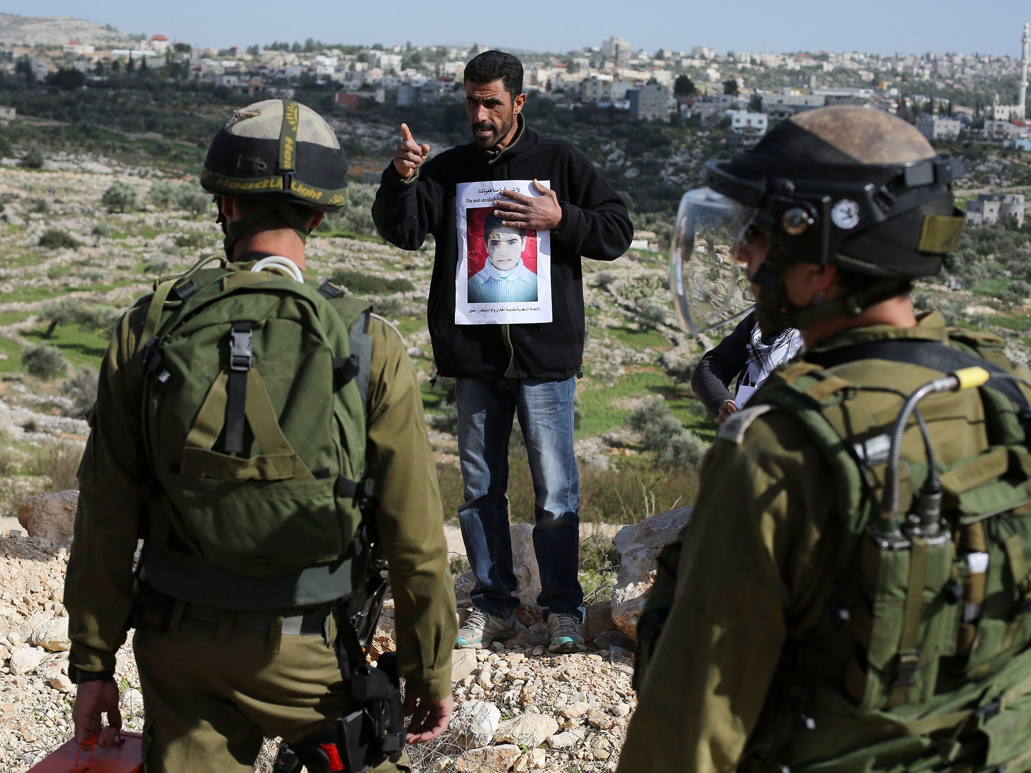 A Palestinian protester from the West Bank village of Bilin shouts in front of Israeli soldiers showing a portrait of Malak al-Khatib on 30 January