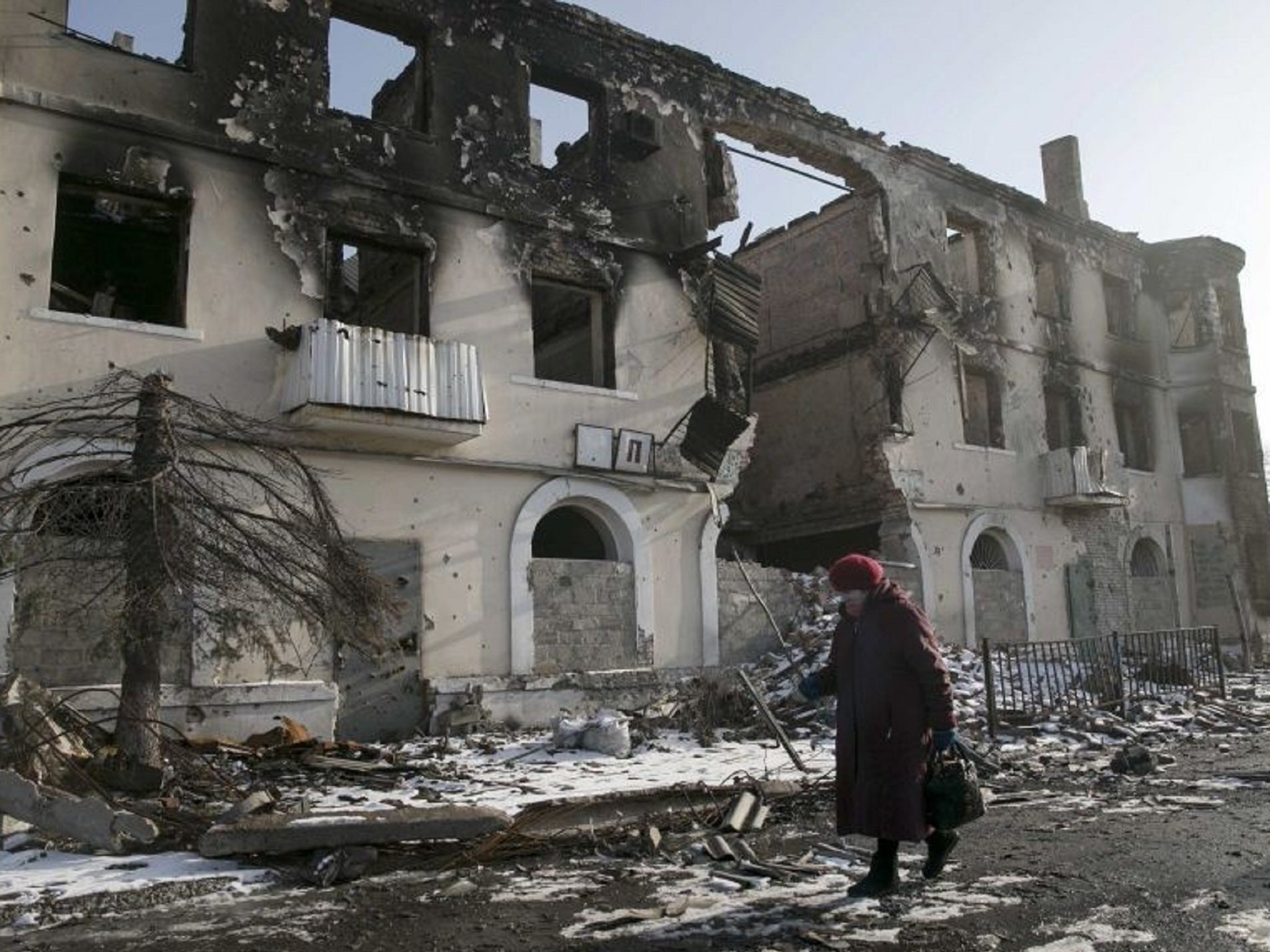 A woman walks past a damaged building in the town of Vuhlehirsk