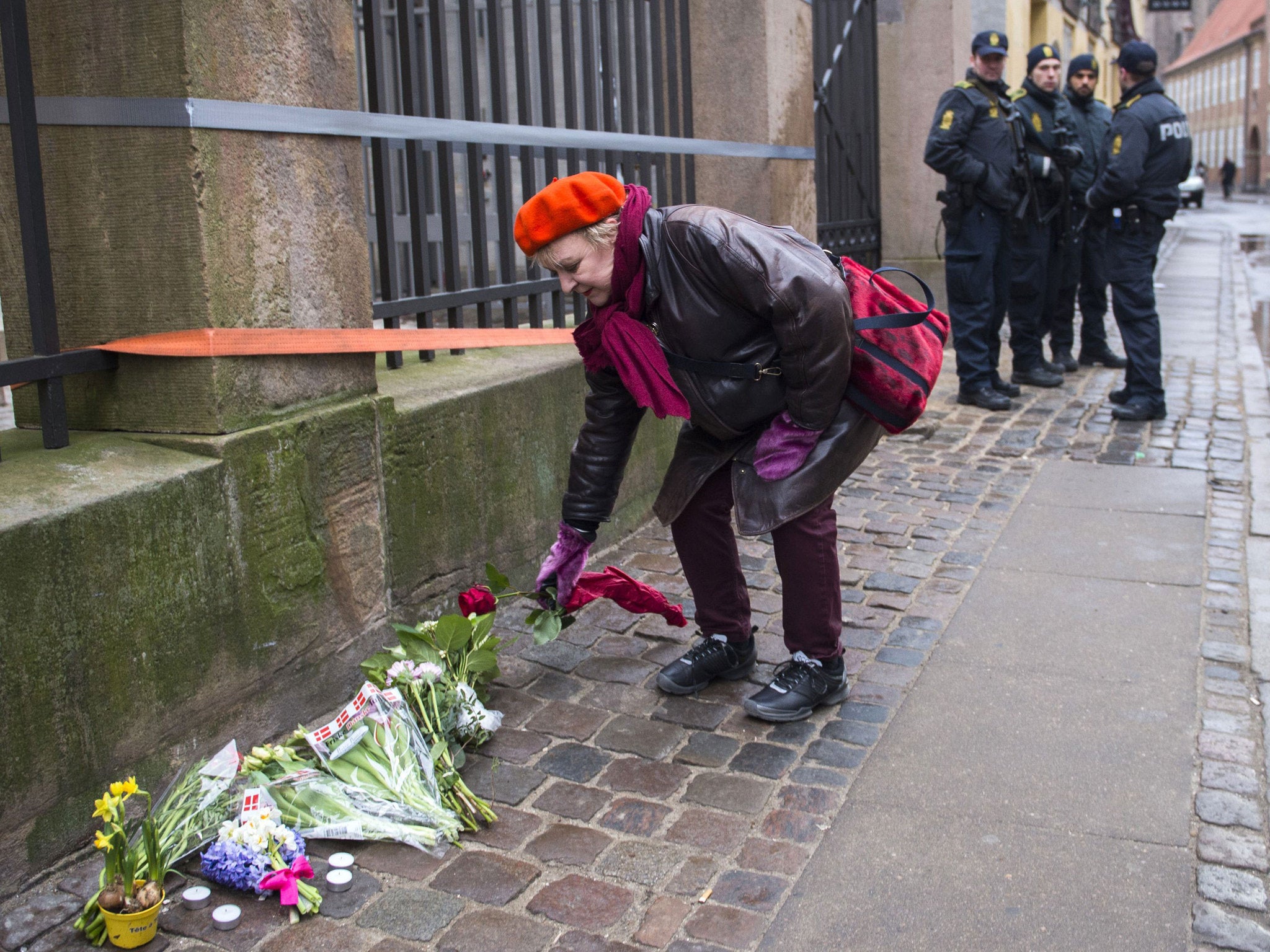 A woman lays flowers outside a synagogue as police officers stand guard in Copenhagen