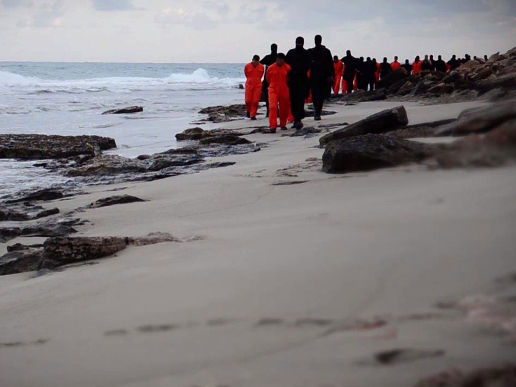 An image from a video released by the jihadist media arm Al-Hayat Media Centre purportedly shows black-clad Islamic State (IS) group fighters leading handcuffed hostages, said to be Egyptian Coptic Christians, wearing orange jumpsuits before their alleged