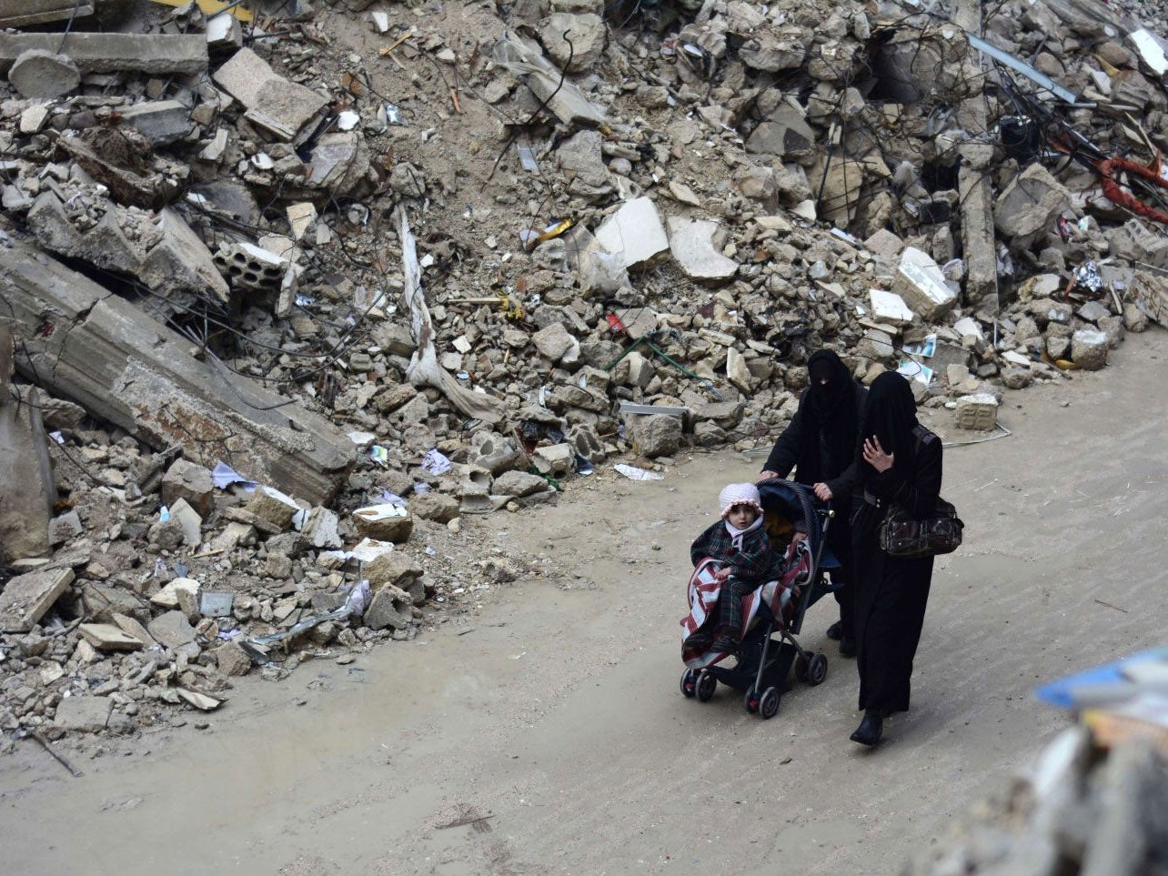 Syrian women walk with a child amid debris on February 13, 2015, following months of shelling by regime forces in the besieged rebel held area of Douma