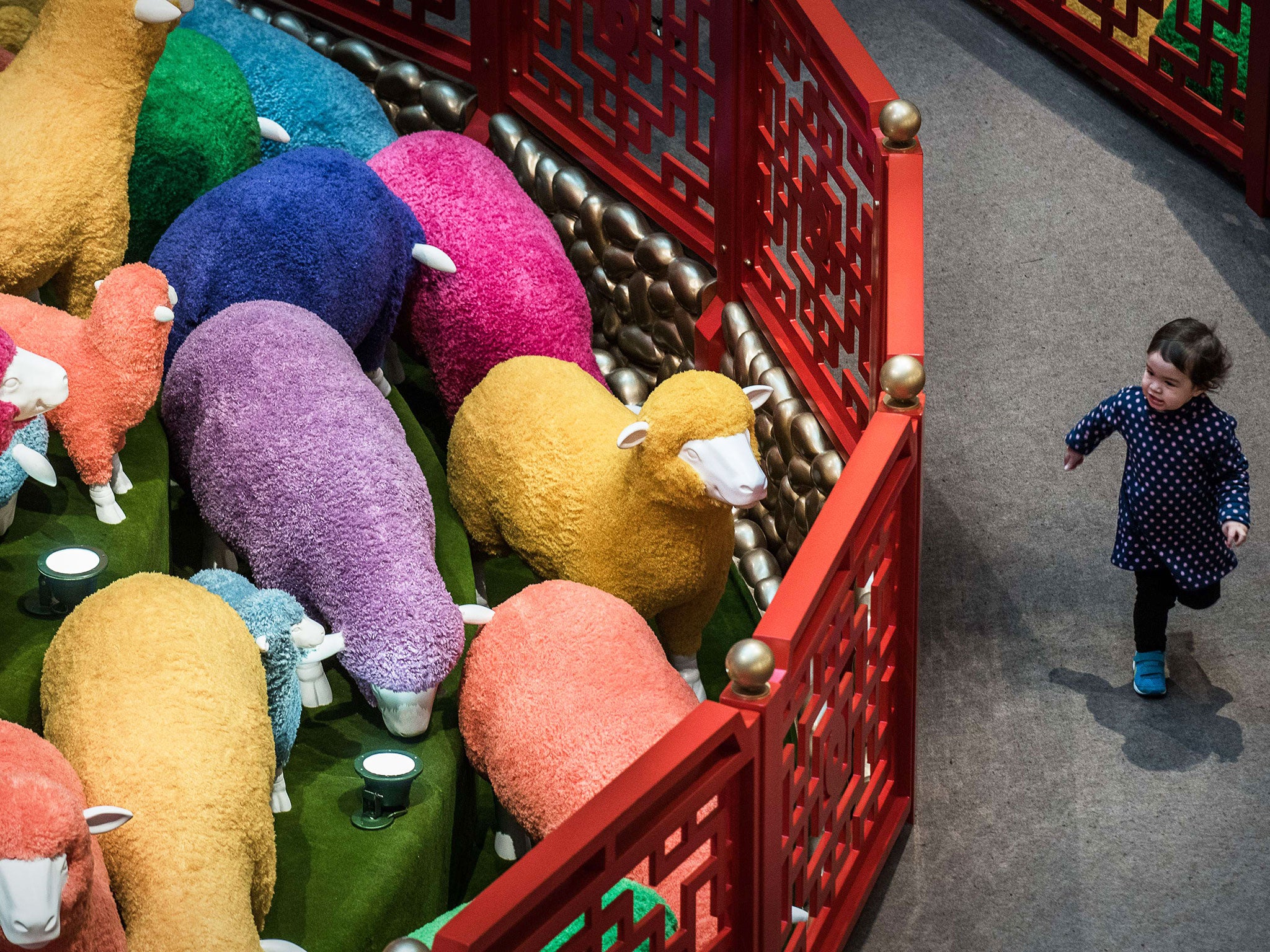 A child runs past a multi coloured sheep installation displayed in a shopping mall for the Chinese New Year celebrations in Hong Kong