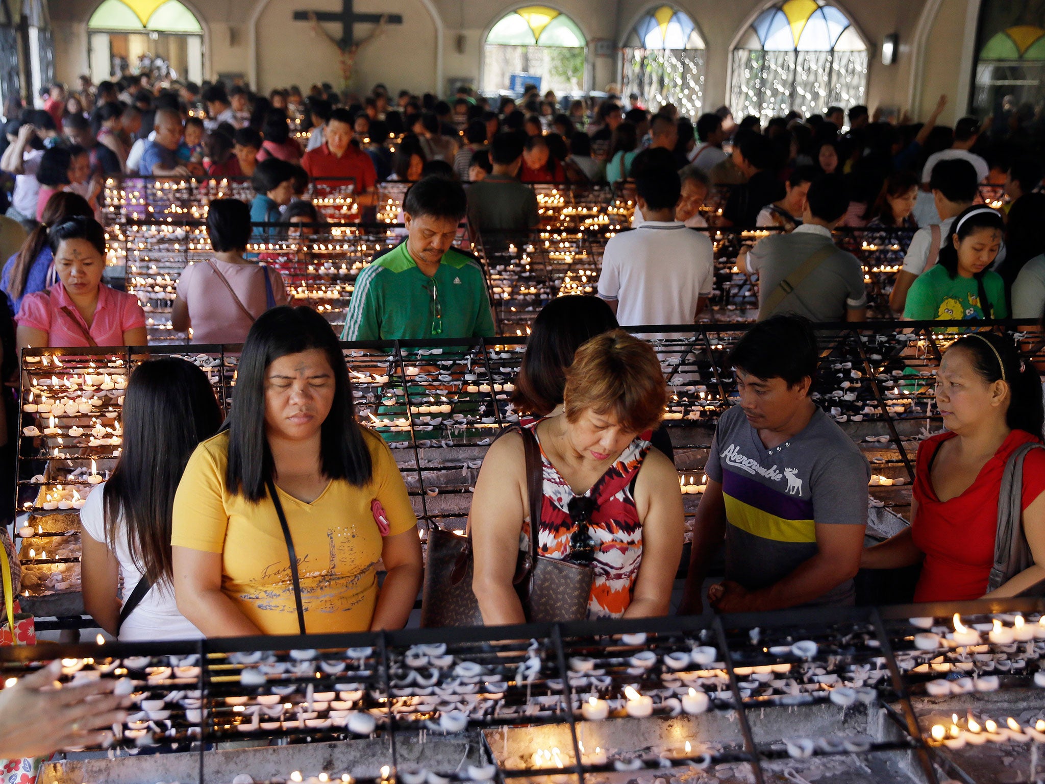 With their foreheads marked with ash, Catholic devotees pray after lighting candles in observance of Ash Wednesday at The Redemptorist Church at suburban Paranaque city, south of Manila, Philippines