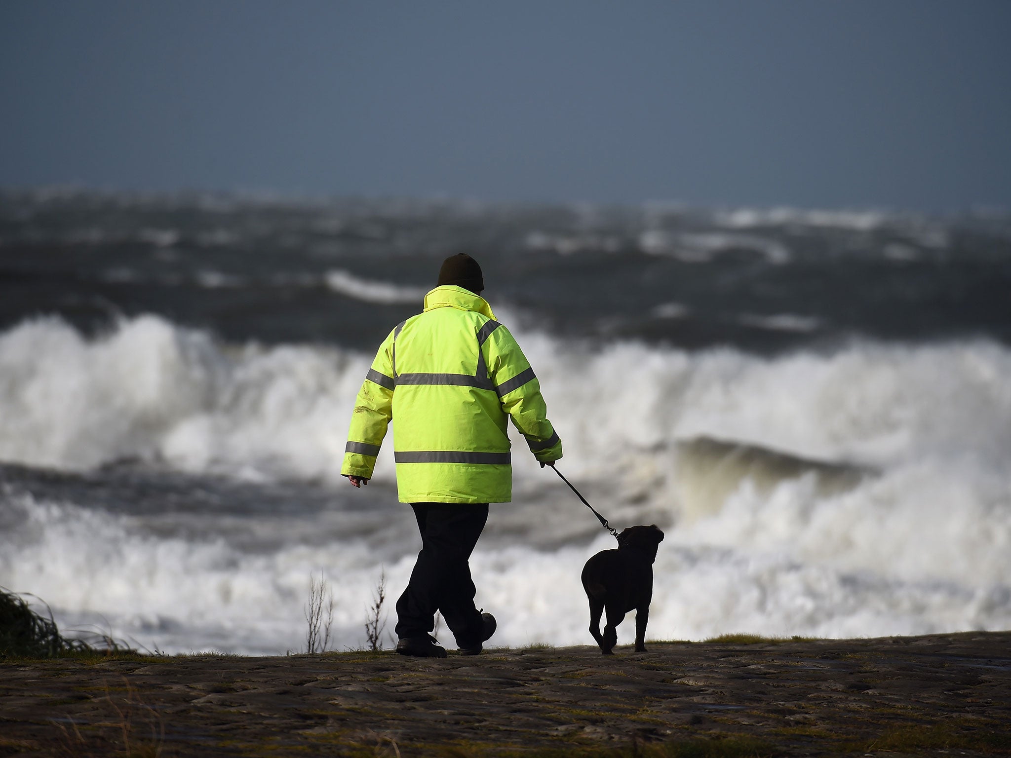 A man walks his dog as the tide comes in.
