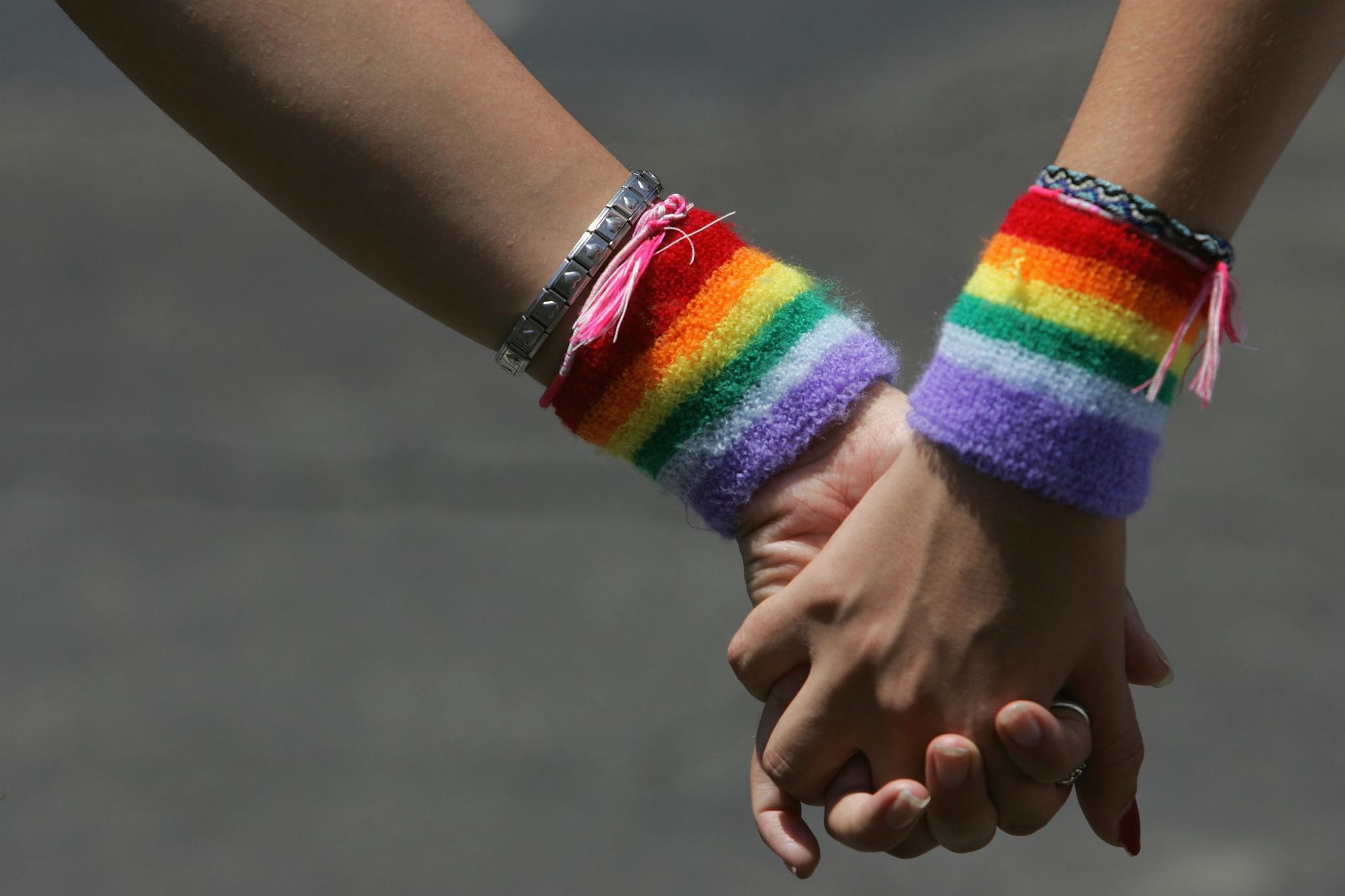 Two women hold hands at a gay pride parade.
