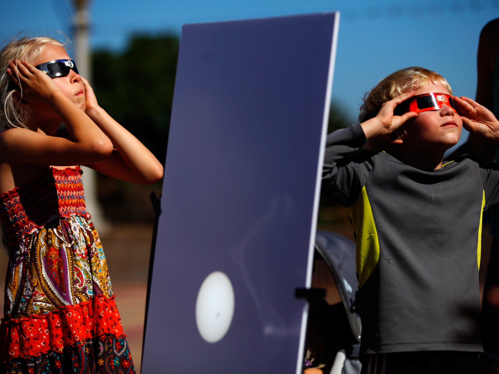 A reflected image of the sun is seen on a white board as kids look up to view the beginning a partial solar eclipse outside the Reuben H. Fleet Science Center in San Diego, California October 23, 2014