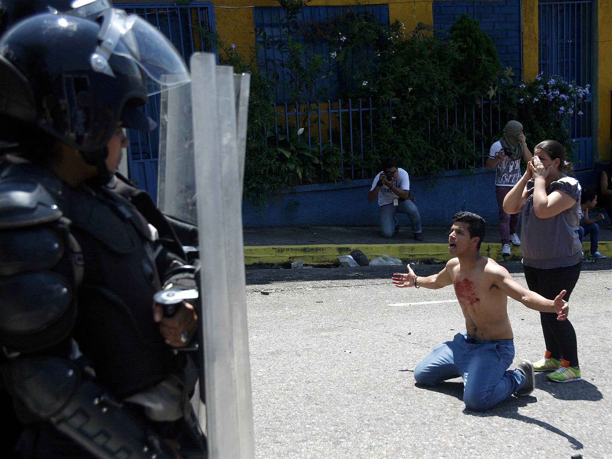 A boy with blood on his chest kneels in front of police after 14-year-old student Kluiver Roa died during a protest in San Cristobal