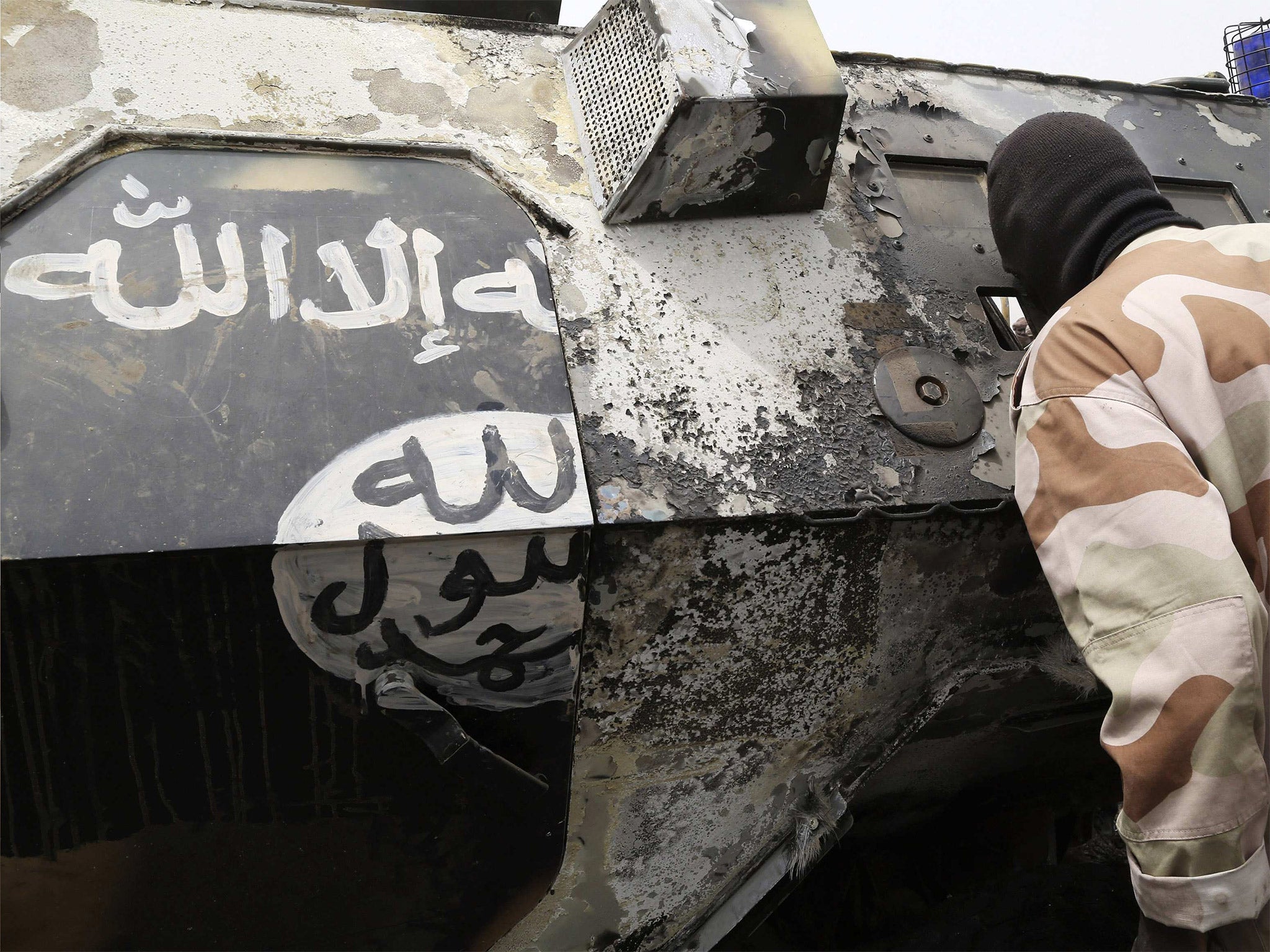 A Chadian soldier peers into a burnt armoured vehicle displaying the black and white markings of insurgent group Boko Haram, after the Chadians destroyed it during a battle in Gambaru