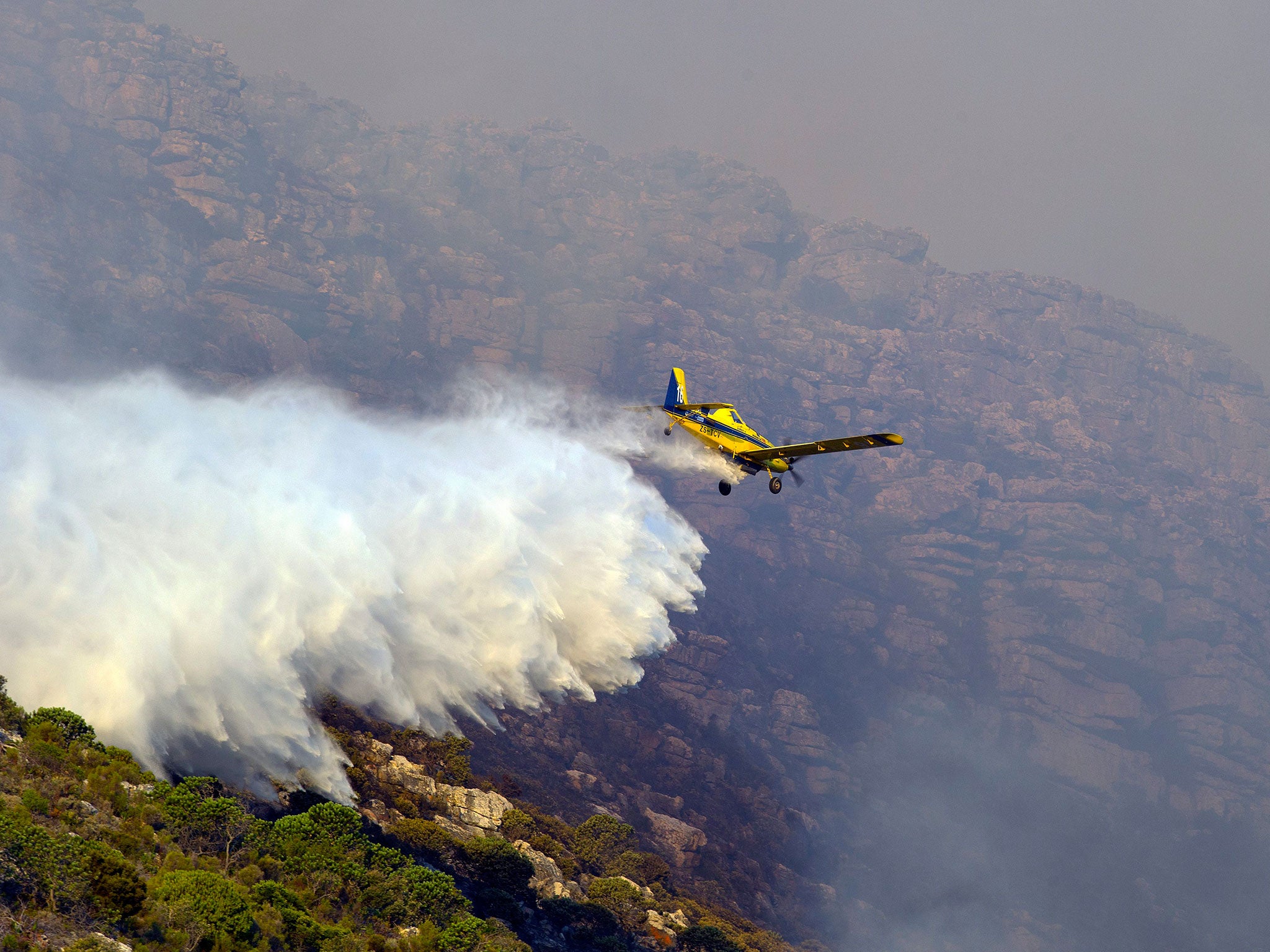 A fire fighting aeroplane bombs water onto an indigeneous Fynbos vegetation fire raging in Clovelly, Cape Town