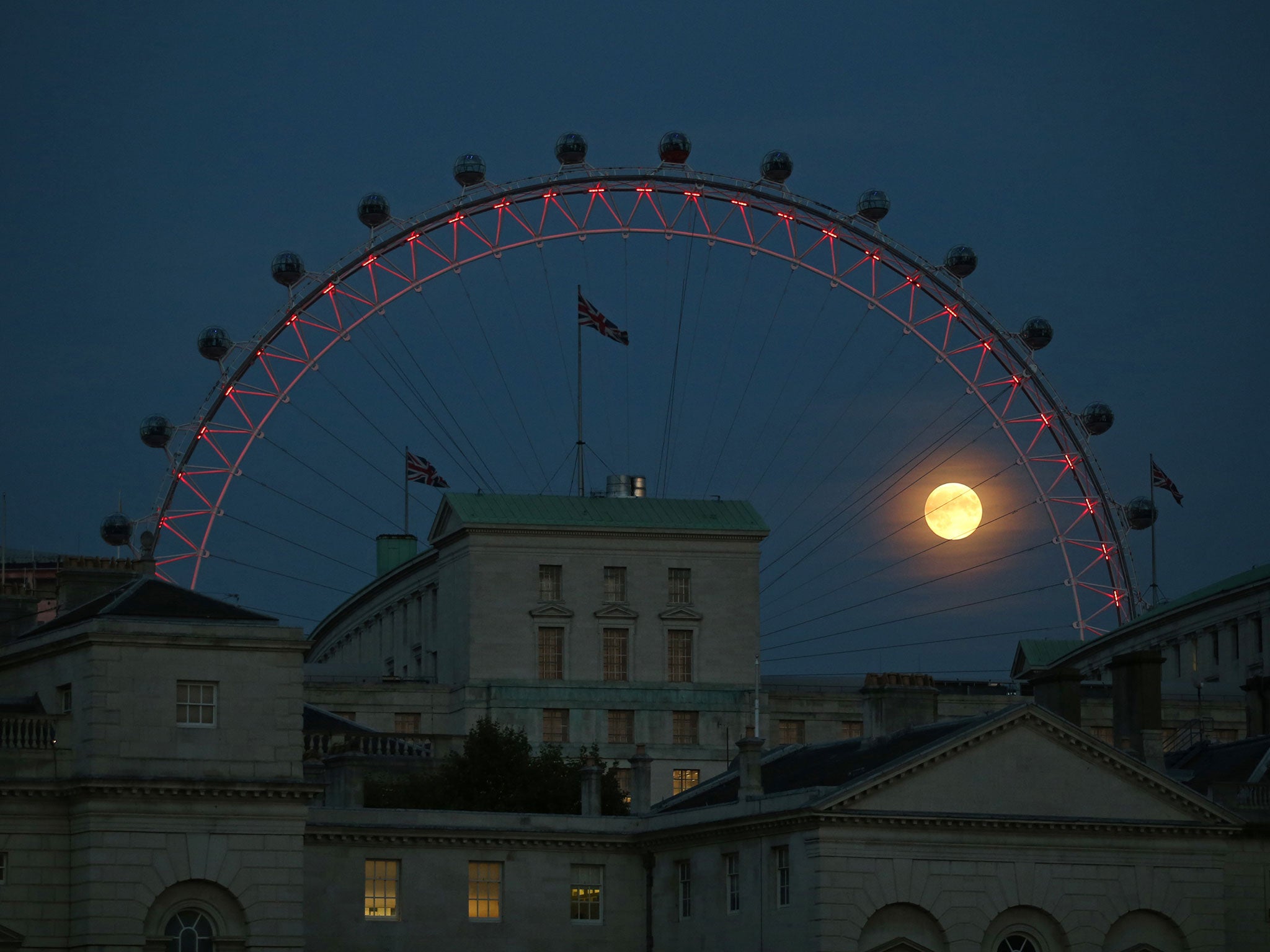 The near full moon is glimpsed through The London Eye ferris wheel view over Whitehall on September 8, 2014 in London, England.