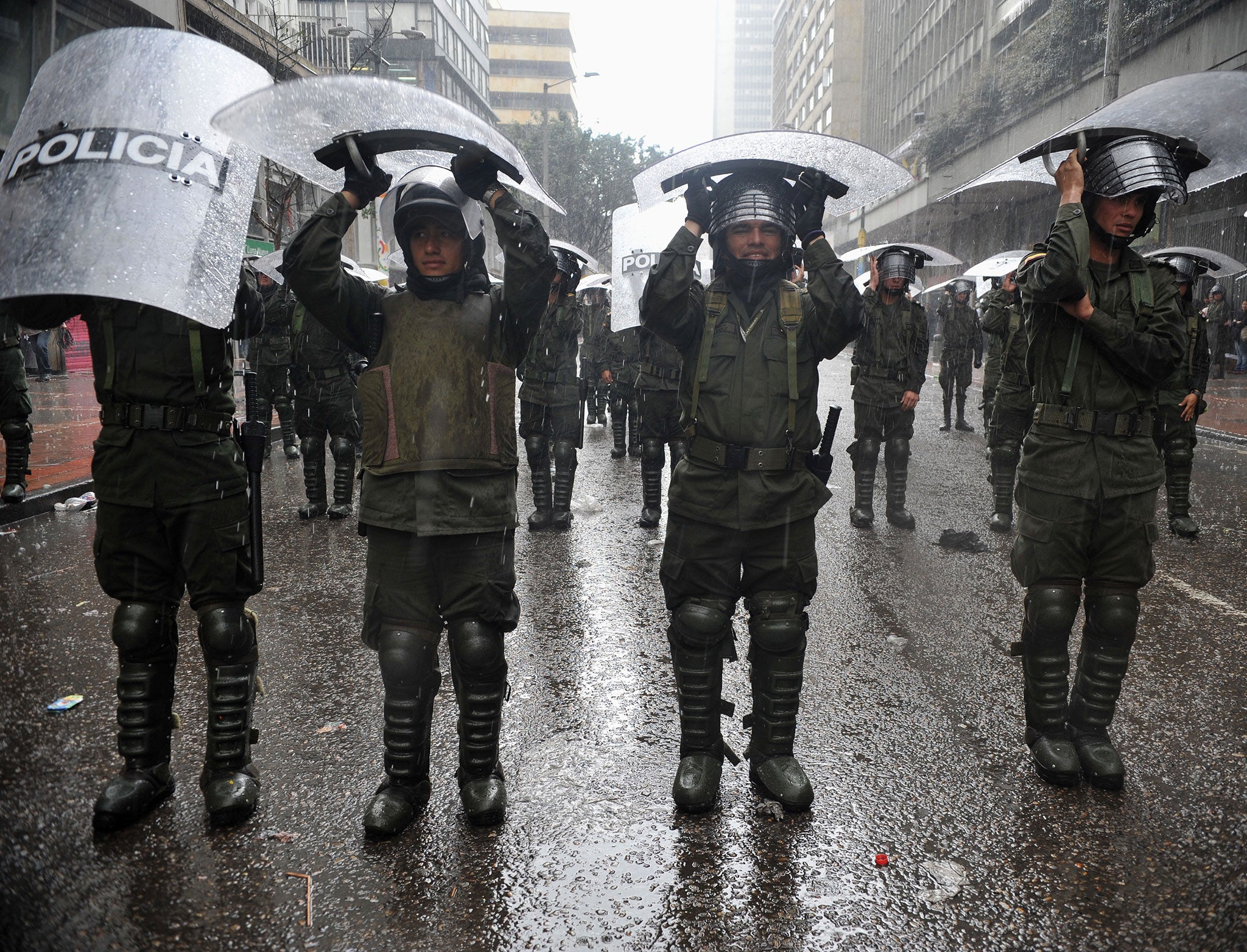 Riot police officers shelter from the rain under their shields