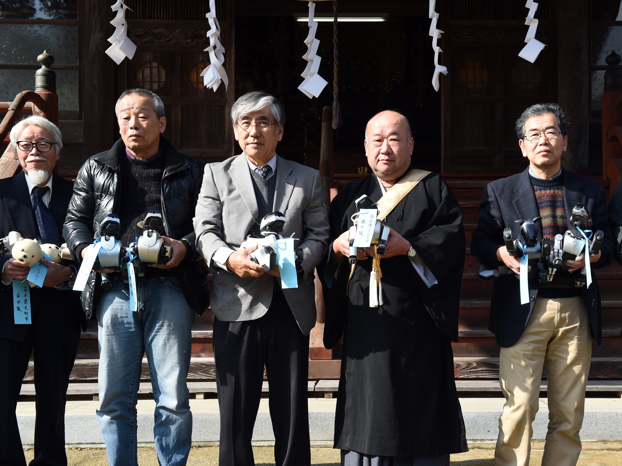 Kofuku-ji temple chief priest Bungen Oi (3rd R), A-Fun president Nobuyuki Norimatsu (3rd L), A-Fun supervisor Hiroshi Funabashi (2nd R) and other A-Fun employee hold Sony's pet robot AIBOs prior to holding the robots' funeral at the Kofuku-ji temple in Isumi