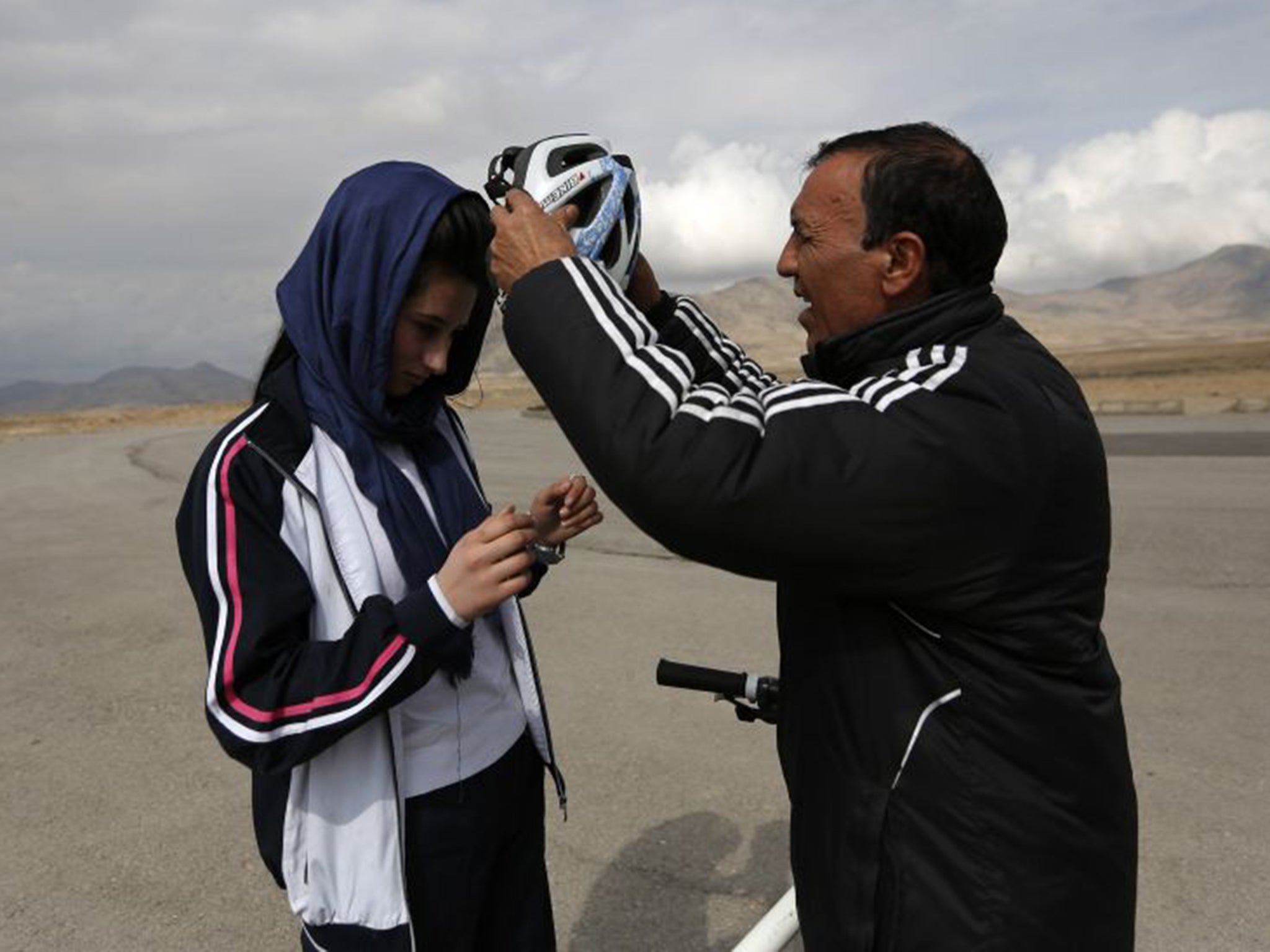 Malika Yousufi, of the Afghanistan's Women's National Cycling Team is helped into her helmet by her coach, Abdul Sadiq Sadiqi, during training on the outskirts of Kabul
