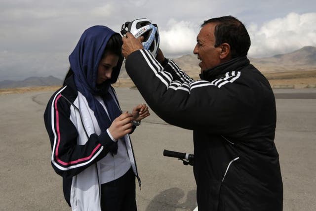 Malika Yousufi, of the Afghanistan's Women's National Cycling Team is helped into her helmet by her coach, Abdul Sadiq Sadiqi, during training on the outskirts of Kabul 