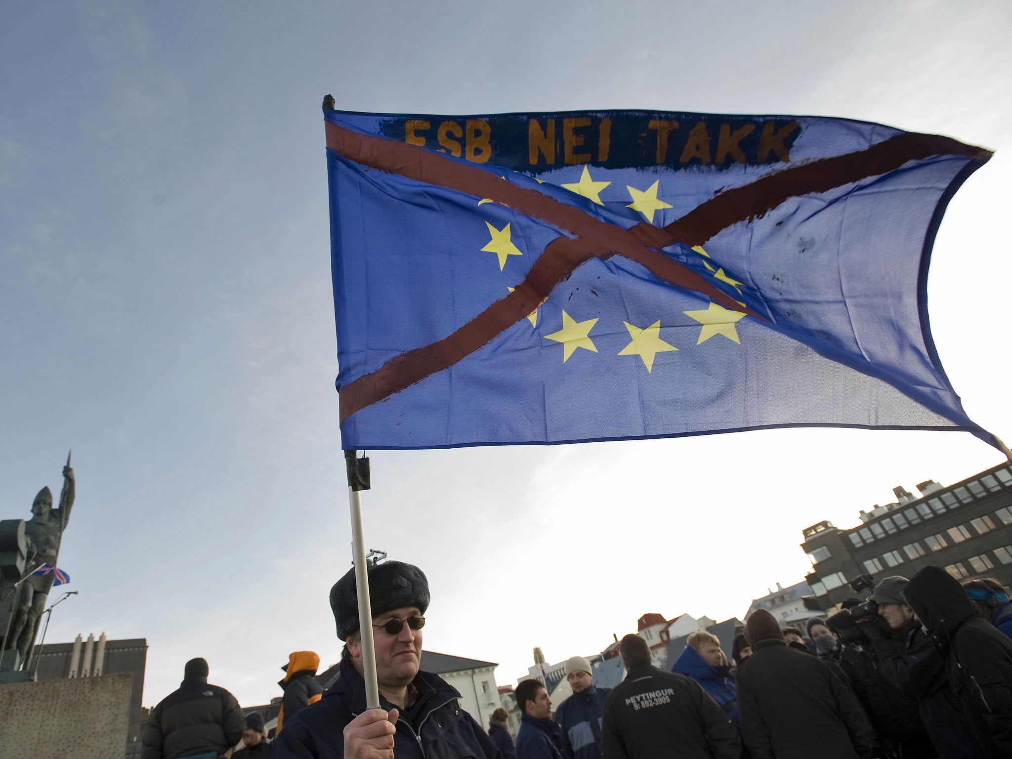 A demonstrator holds an EU flag with a red cross over it in front of the statue of Ingolfur Arnarsson, the founder of Iceland