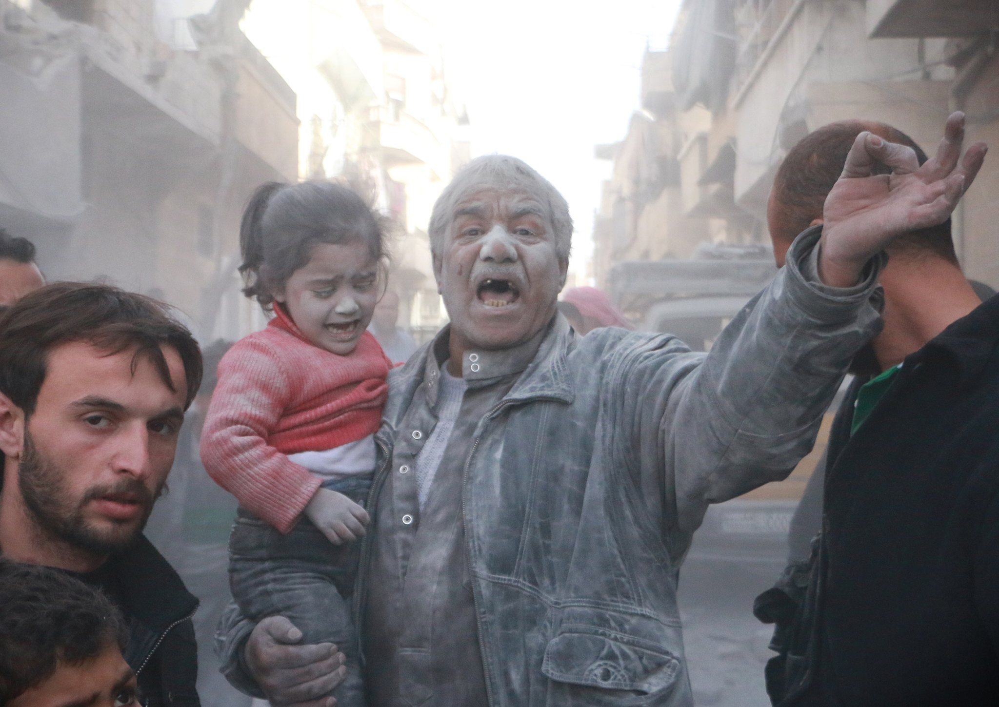 A Syrian man holds a crying girl as he gestures following an air strike by government forces in Aleppo last year