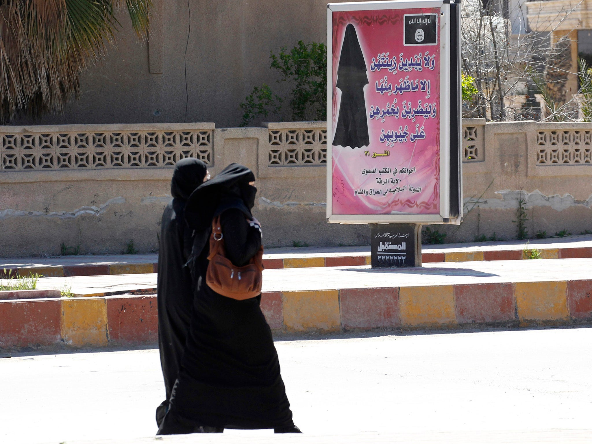 Veiled women walk past a billboard that carries a verse from Koran urging women to wear a hijab in the northern province of Raqqa (REUTERS)