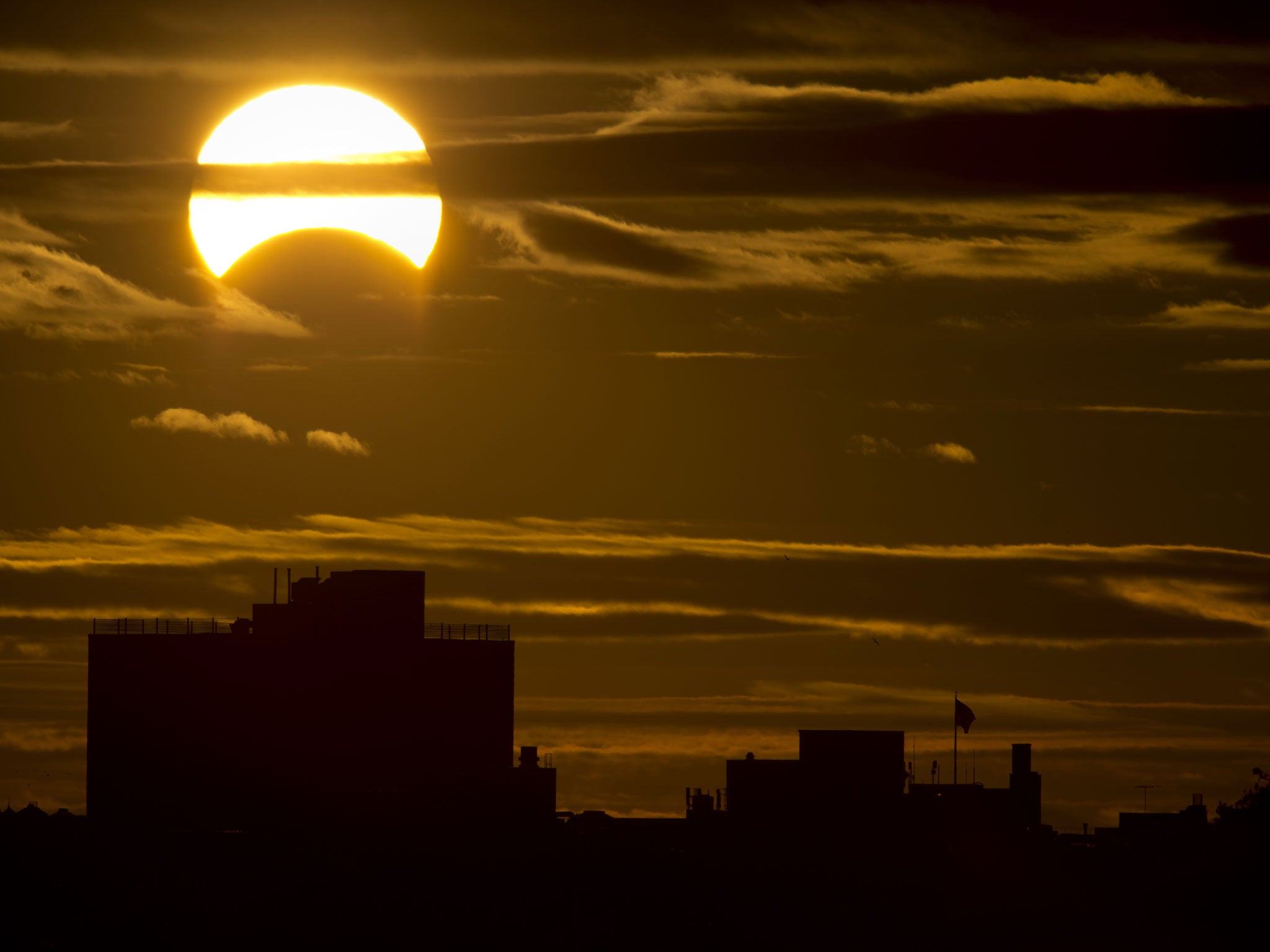 A partial solar eclipse is seen just after sunrise over the Queens borough of New York across the East River