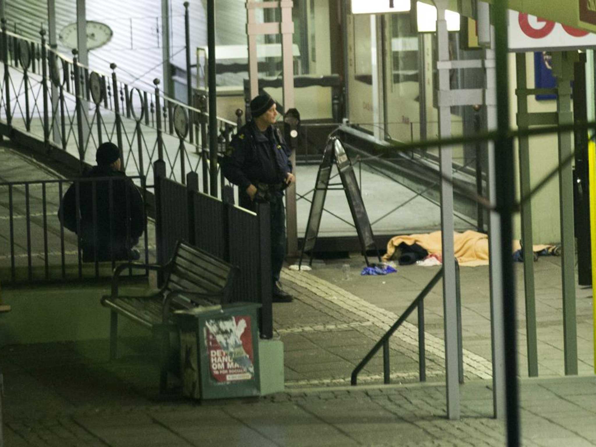 Two Swedish officers outside the scene last night, one of the victims lies covered by a blanket