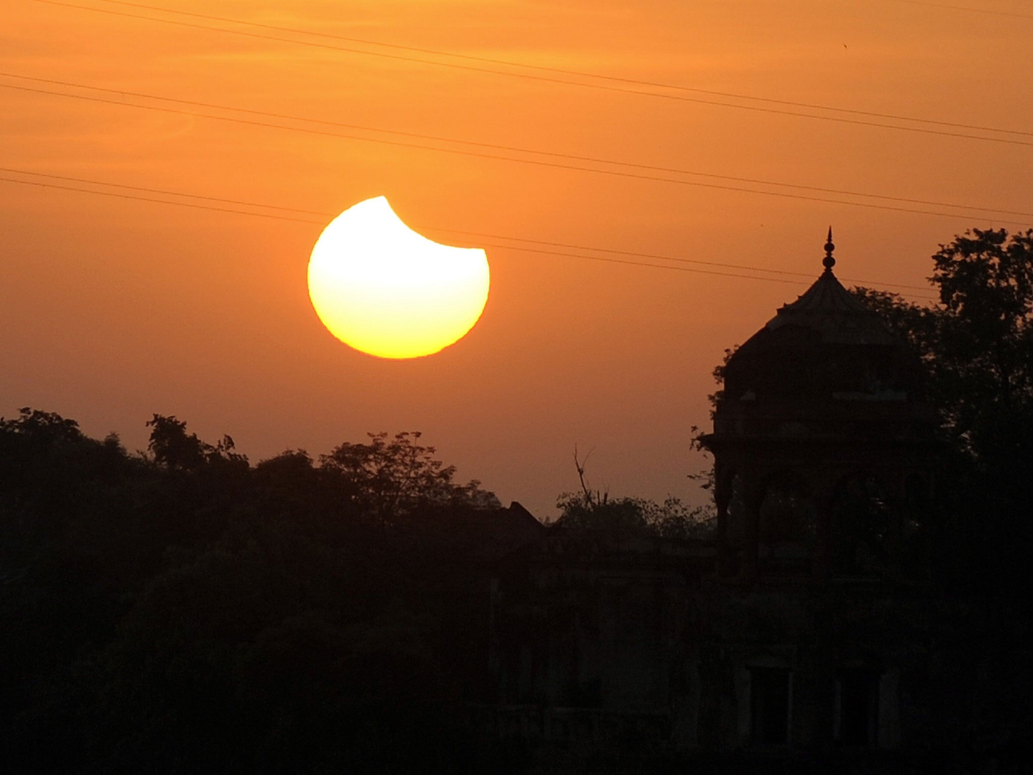 A partial solar eclipse sets over a minaret in Agra, India