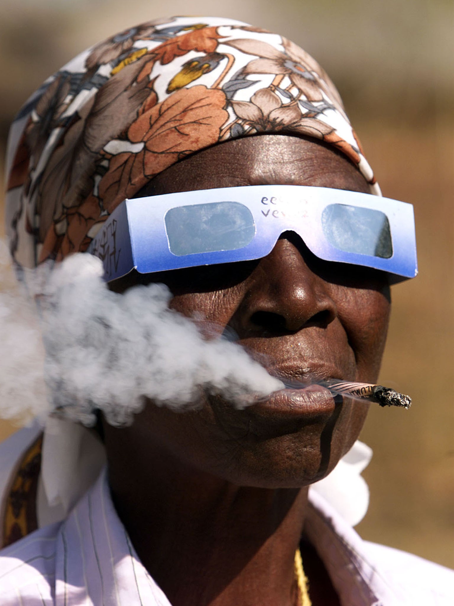 An elderley Zimbabwean woman smokes a hand rolled cigarette while watching the sun shortly before a total solar eclipse in the Mavuradona hills 150 km's north of Harare June 21, 2001