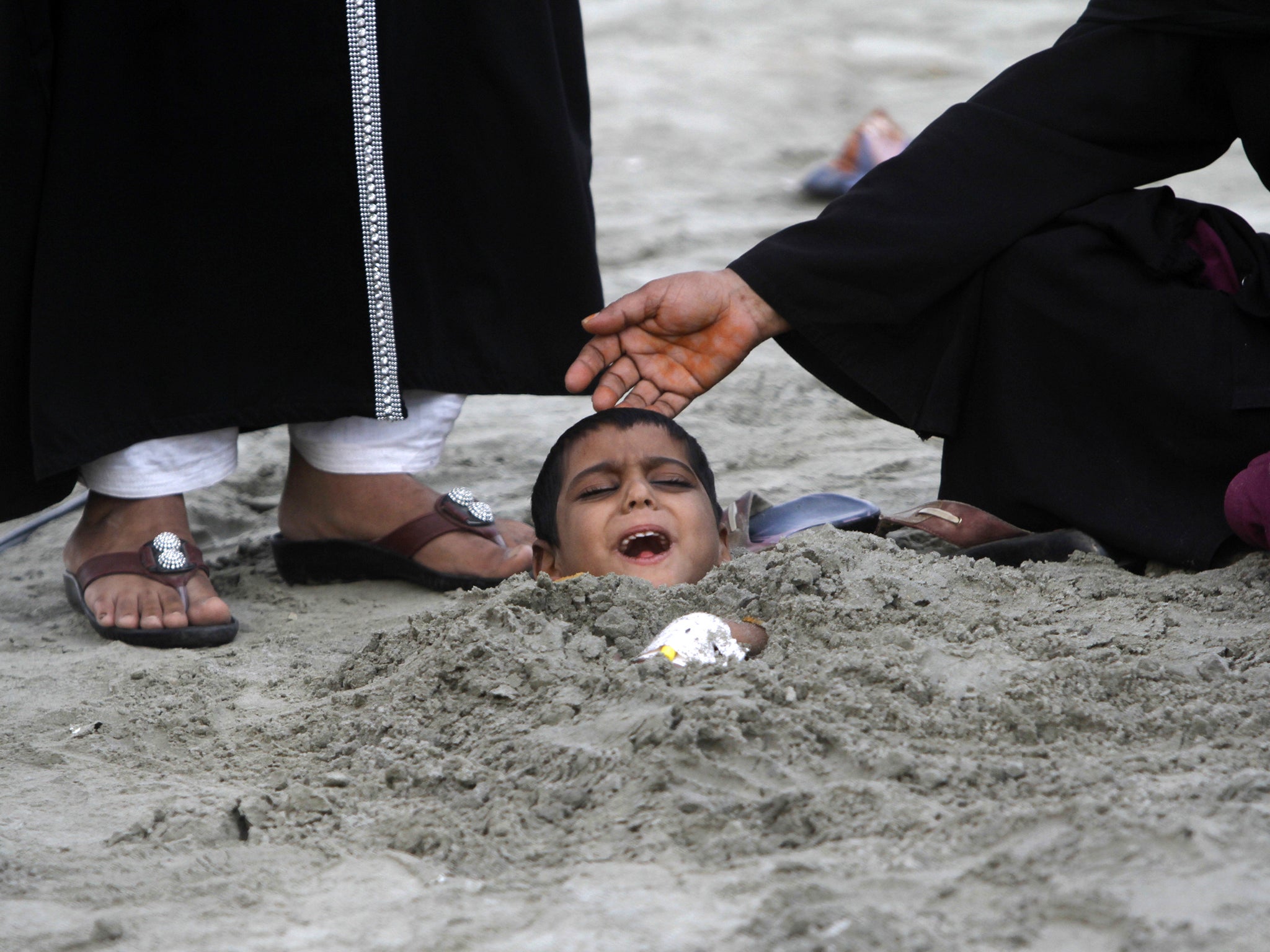 A woman places her hand on her son's head as he lies buried in sand up to his neck during a partial solar eclipse at Karachi's Clifton beach January 4, 2011. Yasir, a seven-year-old handicapped boy, joined people with disabilities who were buried chest-deep during the partial solar eclipse on Tuesday, as part of a traditional superstition that it would bring healing to their bodies