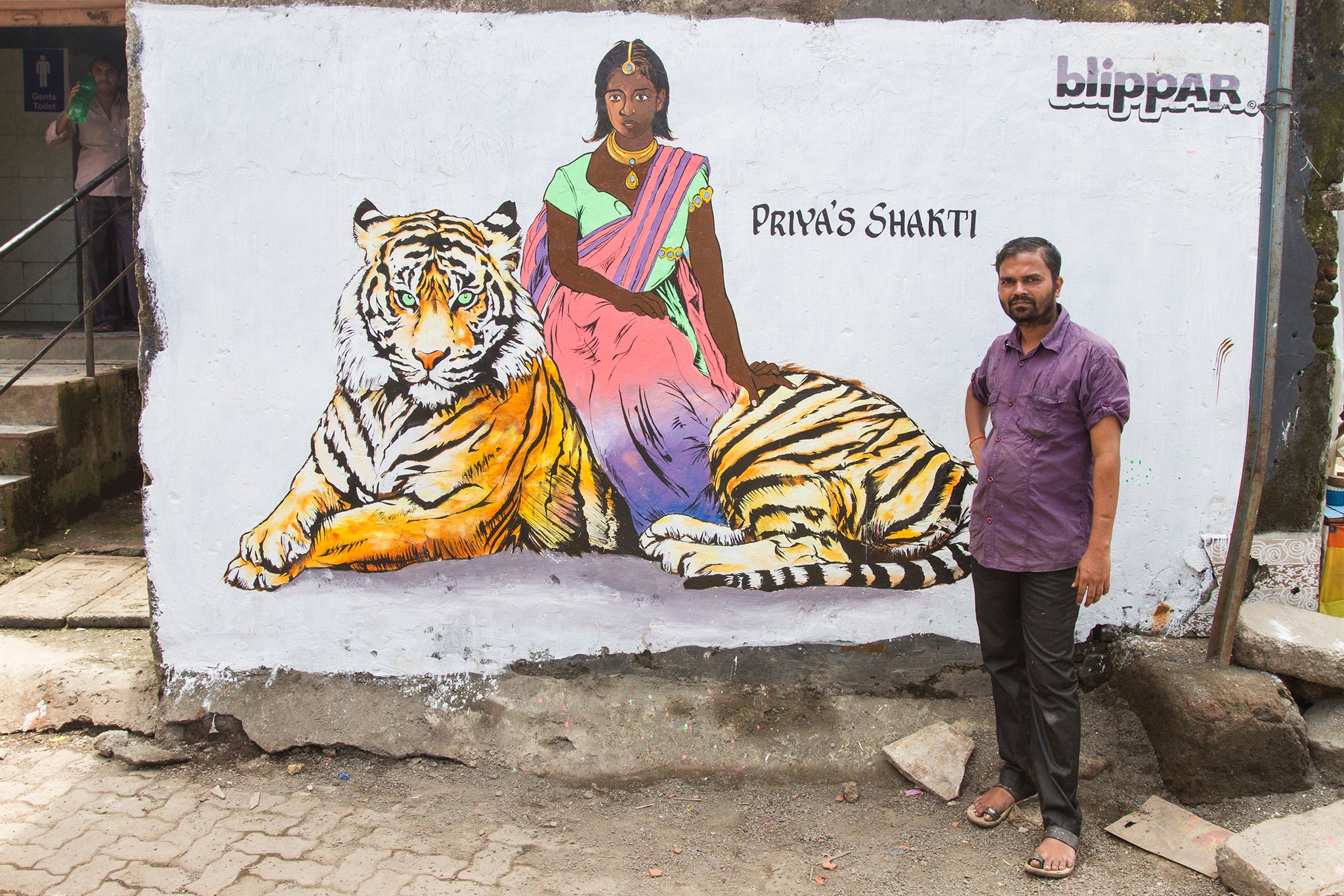 Ram Devineni standing with a mural of Priya