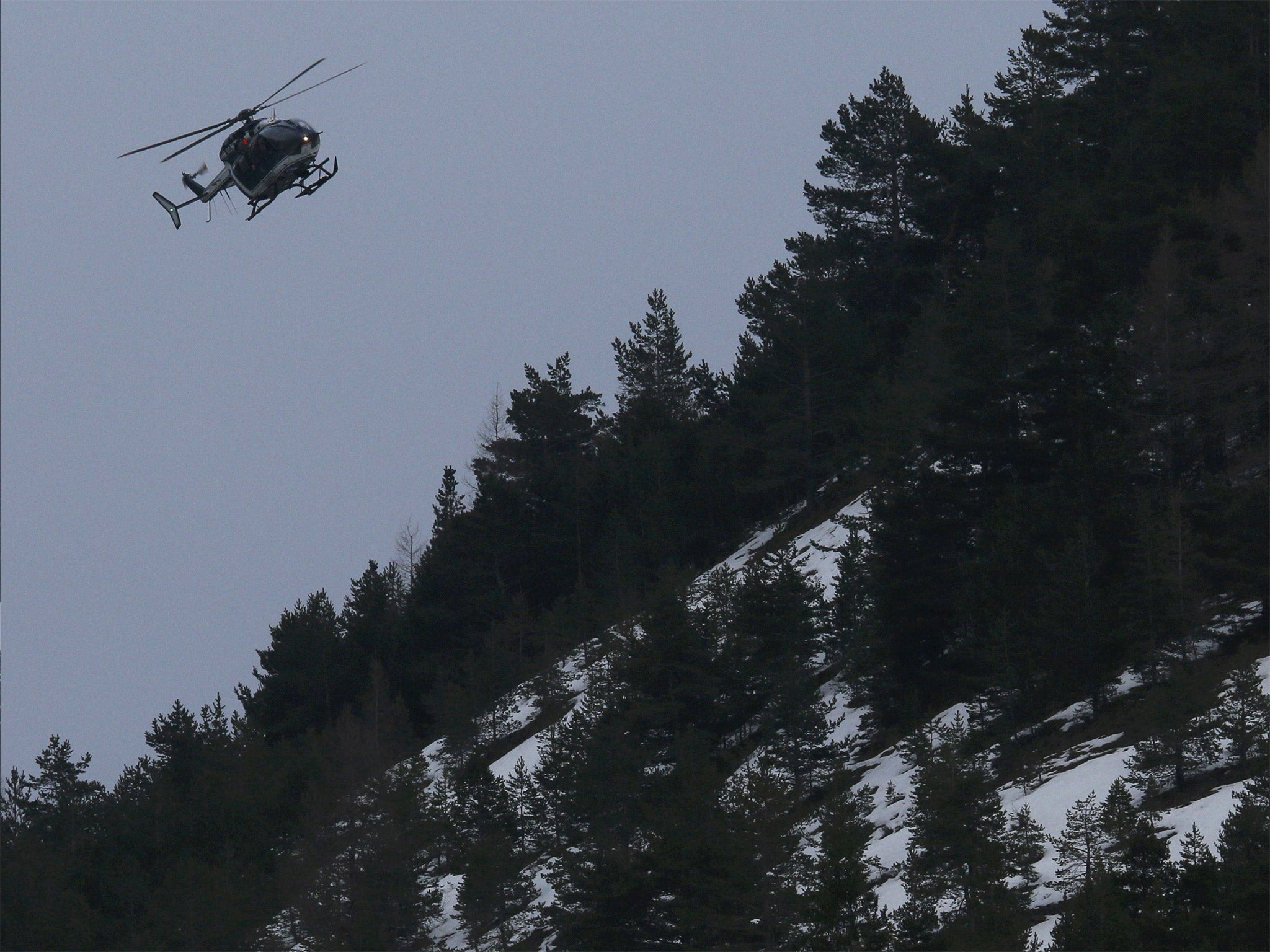 A rescue helicopter from the French Gendarmerie flies over the French Alps, as day fades into night near to the crash site of the Airbus A320