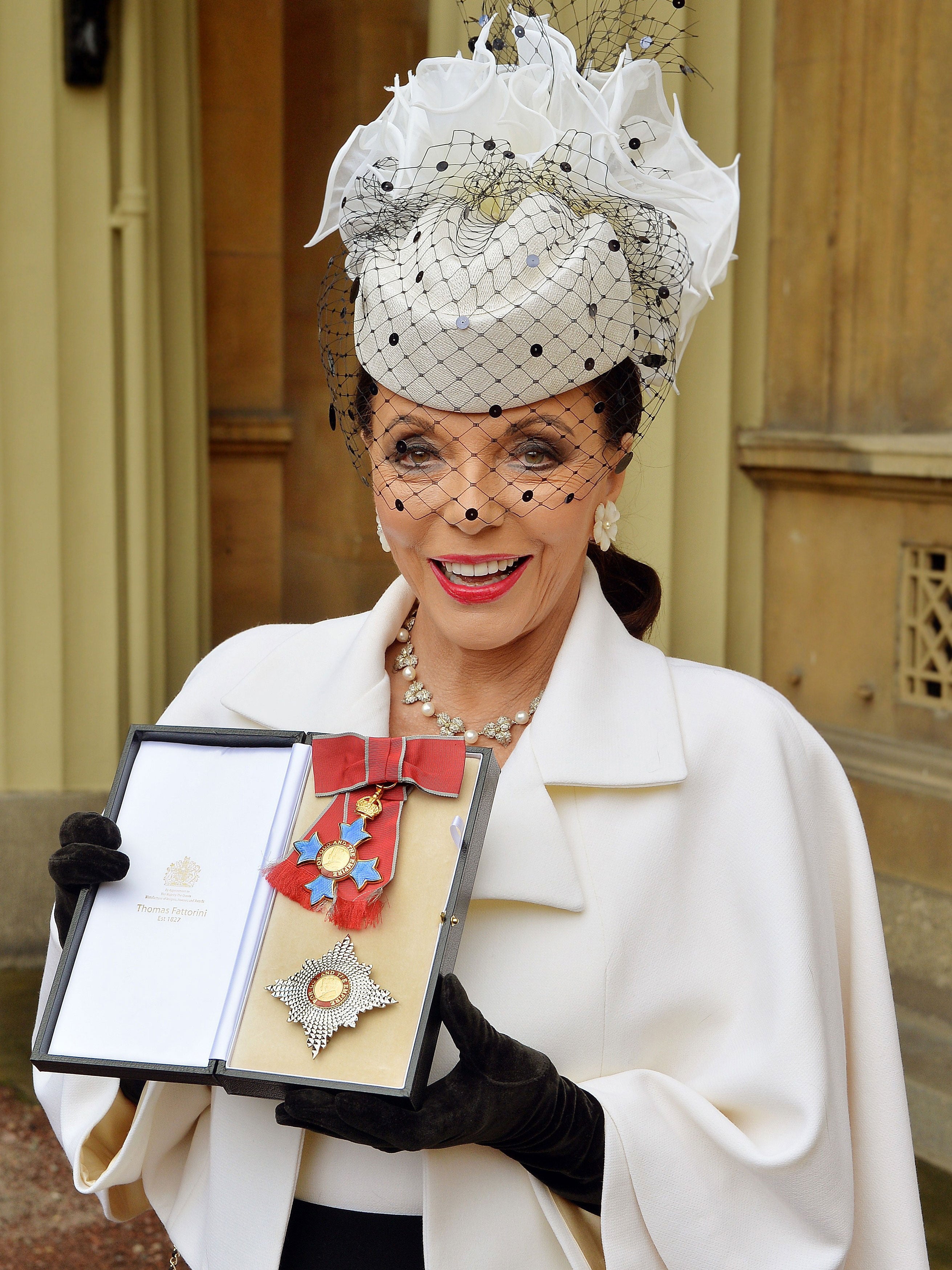 Joan Collins poses for pictures as she holds her insignia of Commander of the Order of the British Empire, (CBE)