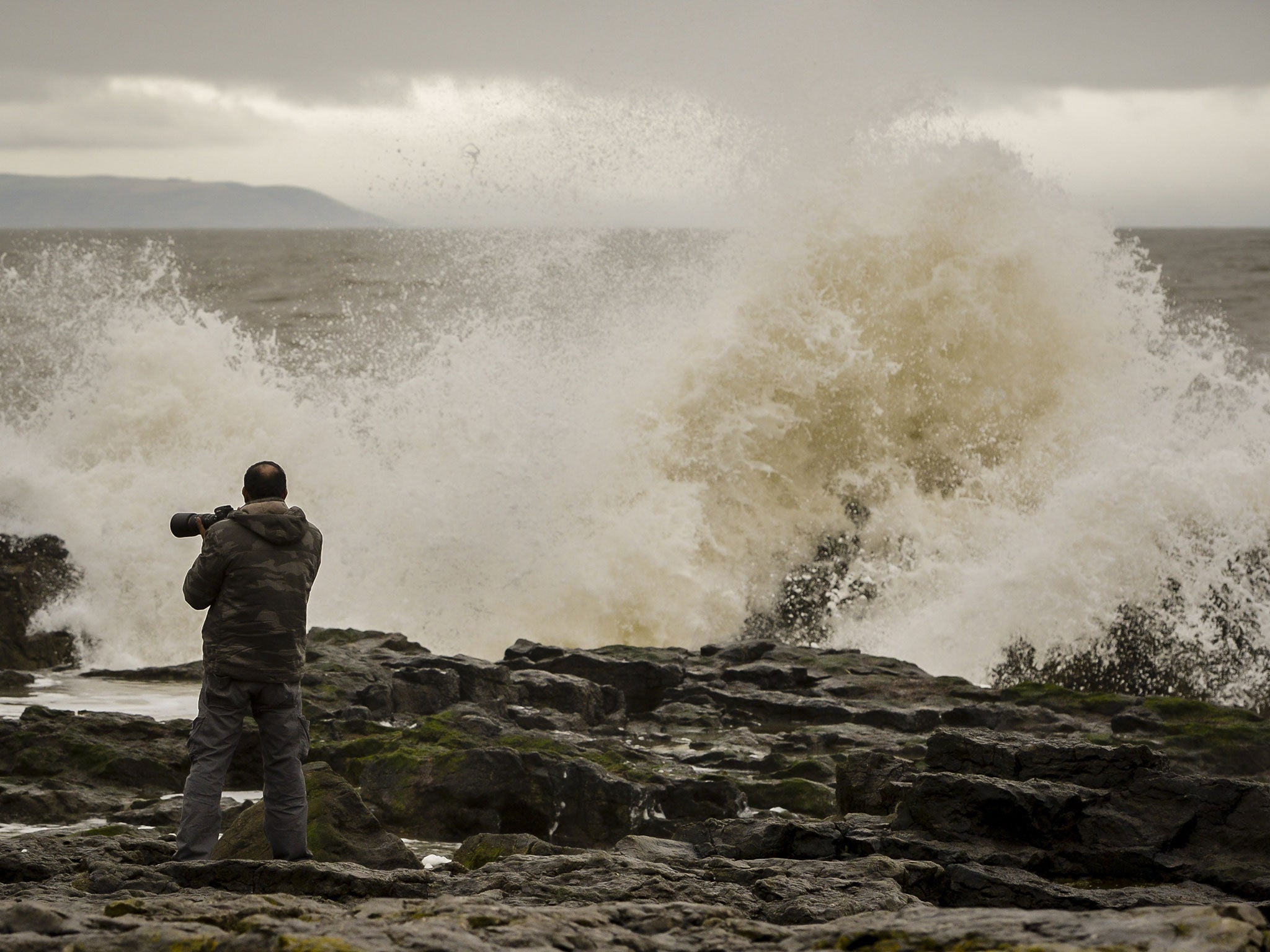 File image: A man photographs waves on Porthcawl Beach in South Wales, as gale force winds and torrential rain sweep across Britain