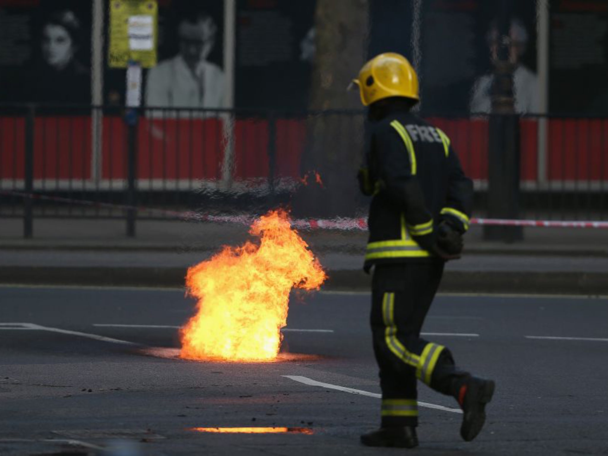 Flames are seen escaping from a manhole cover as fire crews tend to the underground cable fire at Lincoln's Inn Fields