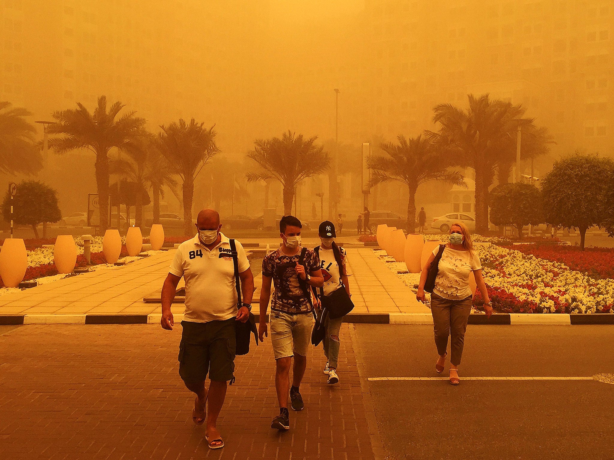 Foreigners wear medical masks as they walk in a street in Dubai amid a sandstorm that engulfed the city