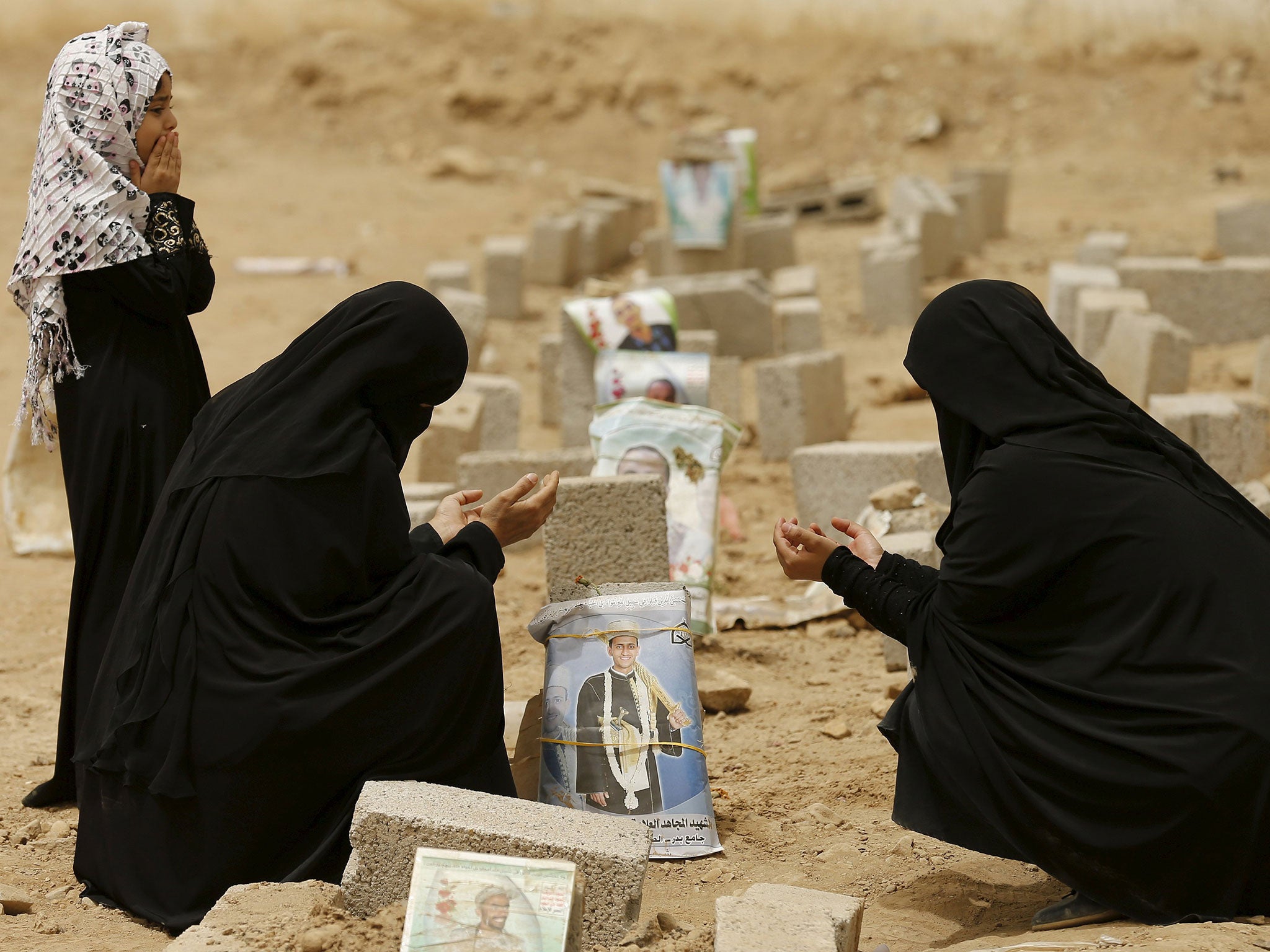 Women pray over the grave of a relative at a cemetery in Sanaa for Houthis killed in Yemen’s conflict