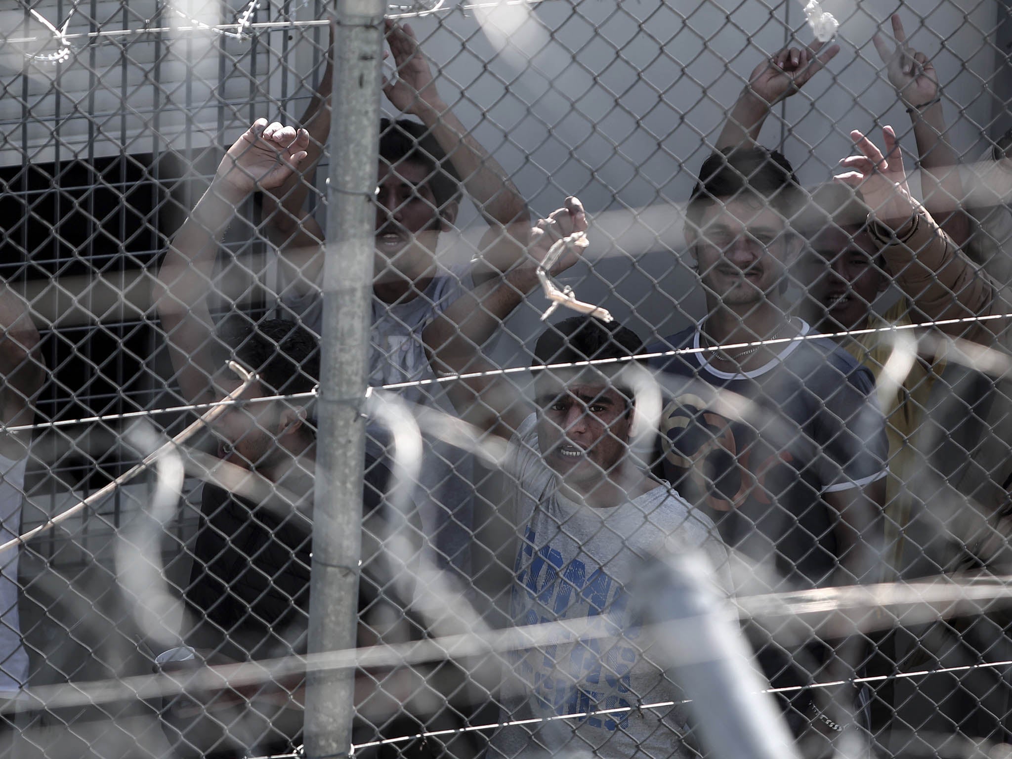 Migrants stand behind a fence at the detention centre for illegal immigrants in Amygdaleza, near Athens